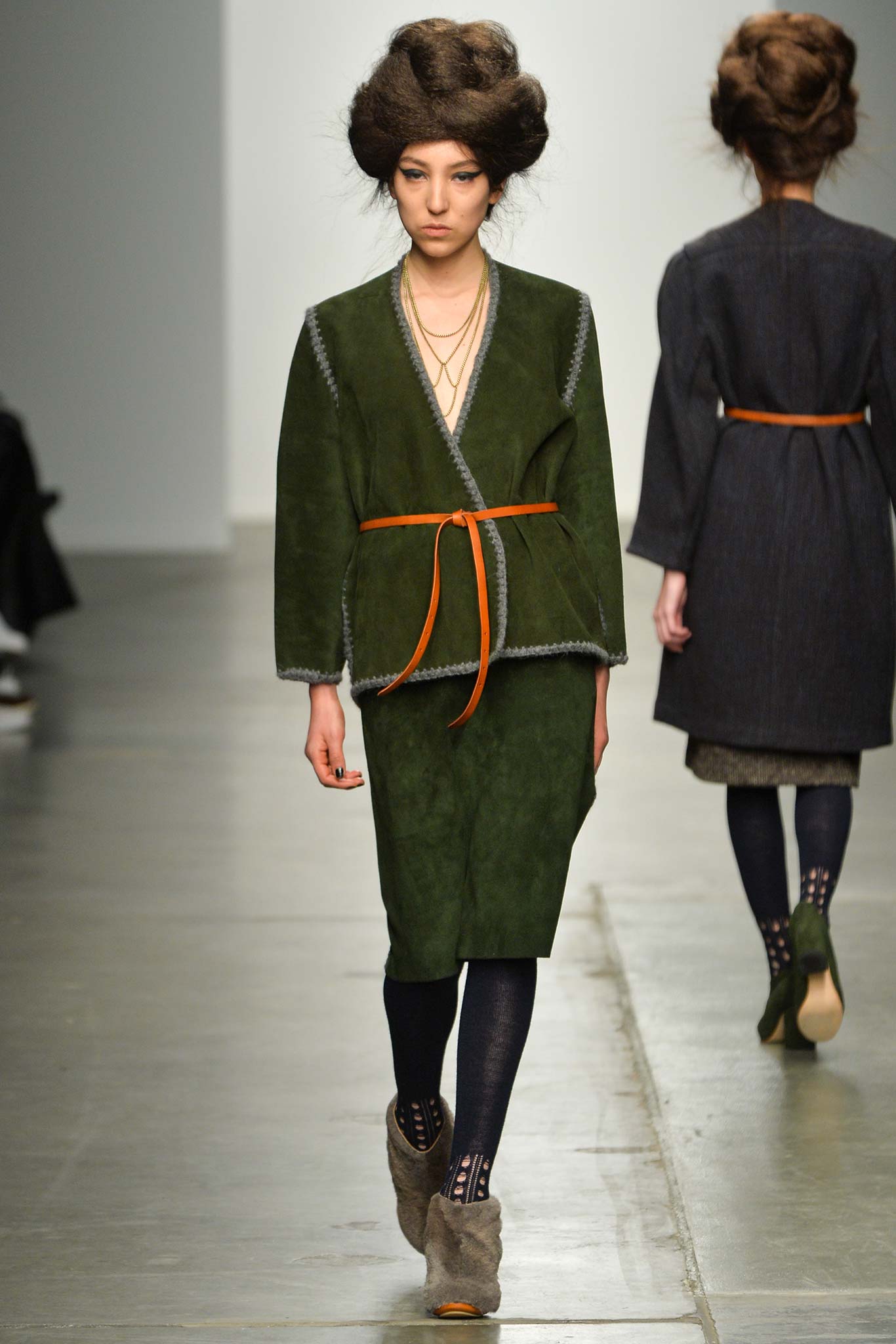 A fitted green suede dress with a belted waist and long sleeves, featuring an asymmetric design.