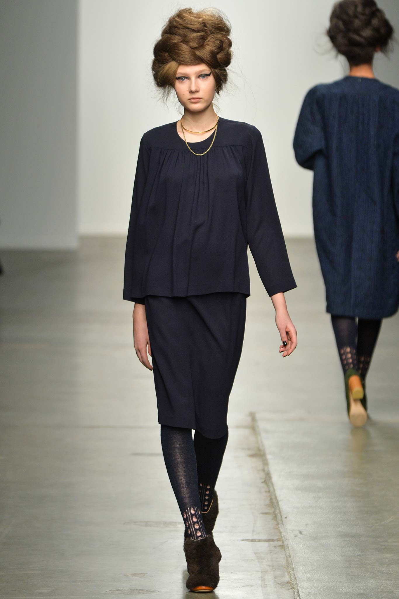 A relaxed black cotton dress with long sleeves, a collared neckline, and pleated details.