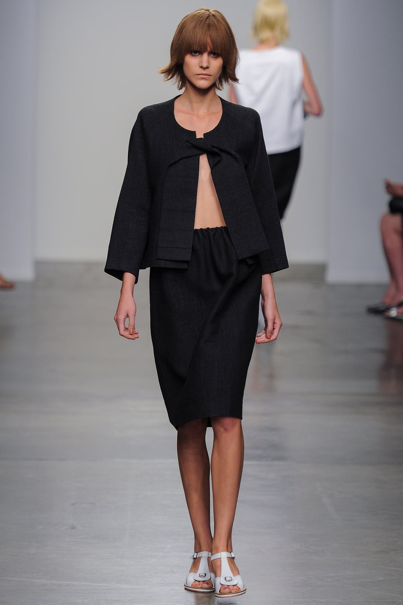 A fitted black cotton jacket with short sleeves and an asymmetric skirt.