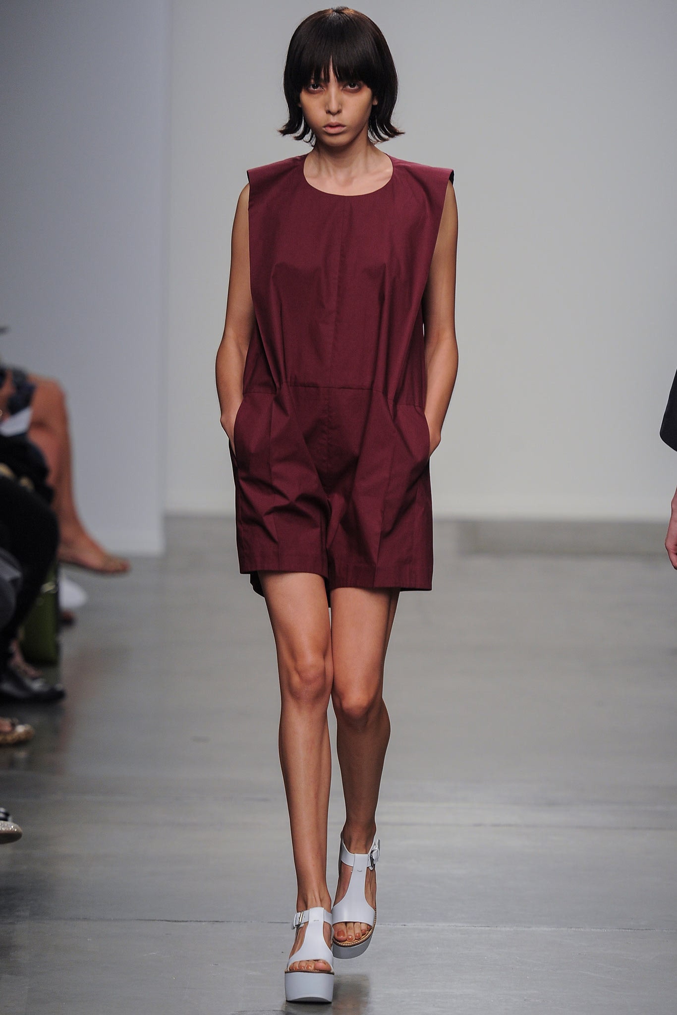 A fitted burgundy sleeveless romper with pleated details and a collared neckline.