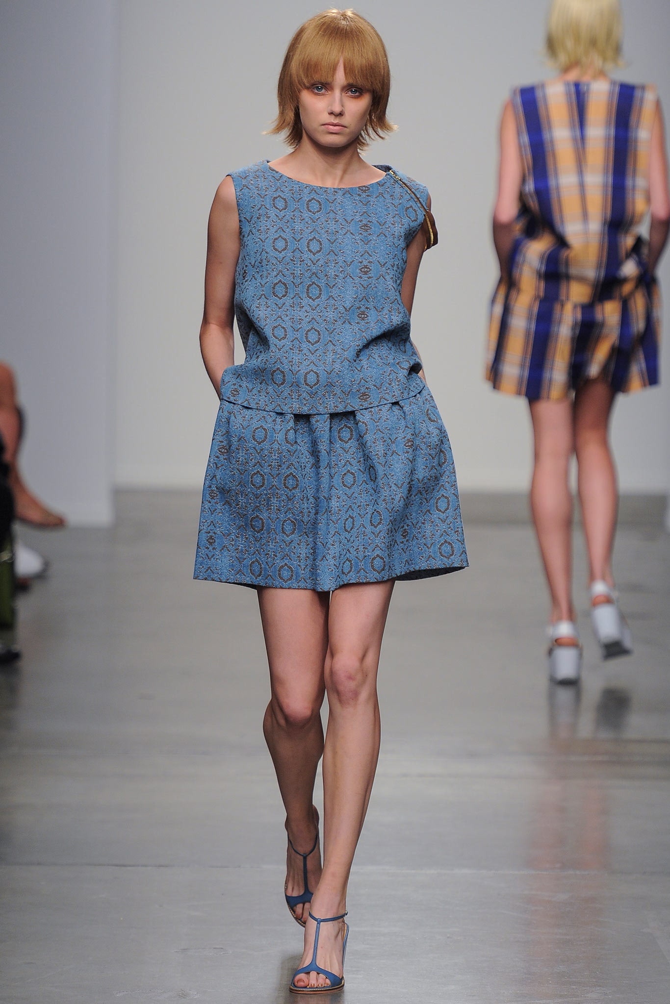 A fitted blue sleeveless dress with a high neckline and printed design.