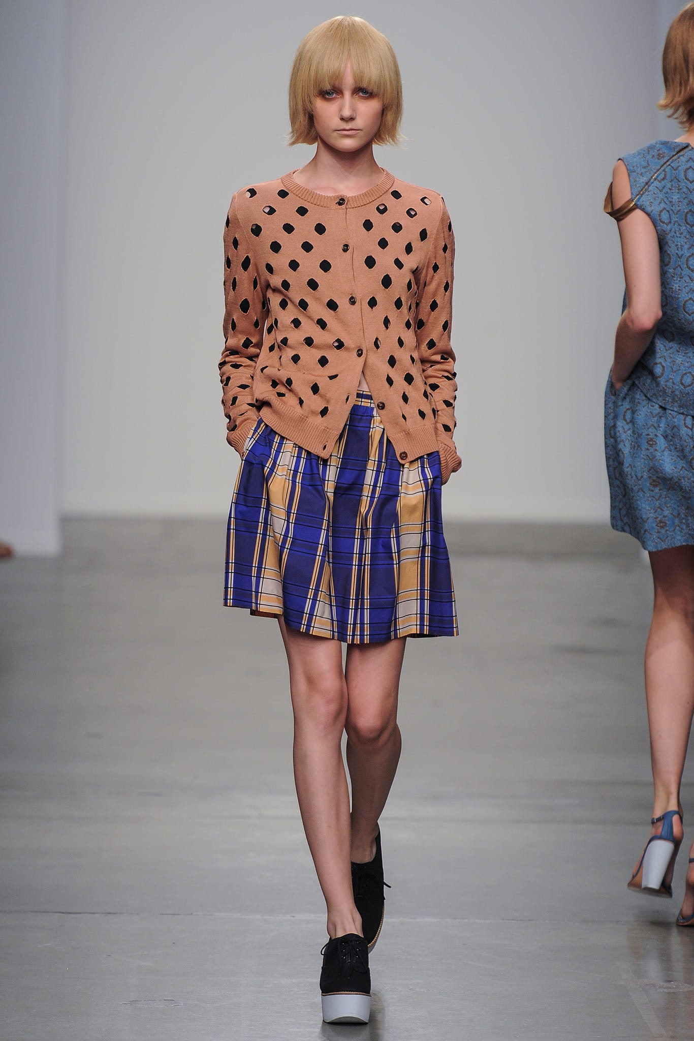 A fitted beige polka-dot cardigan paired with a plaid skirt, showcasing a playful and stylish look.