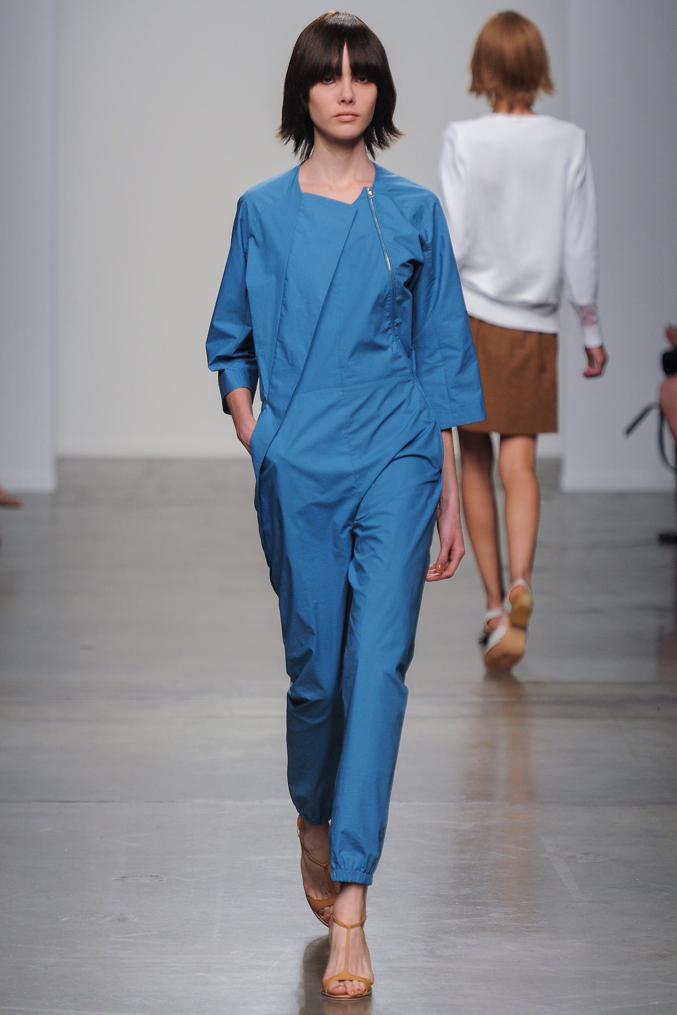 A relaxed blue cotton jumpsuit with long sleeves and a zippered front.