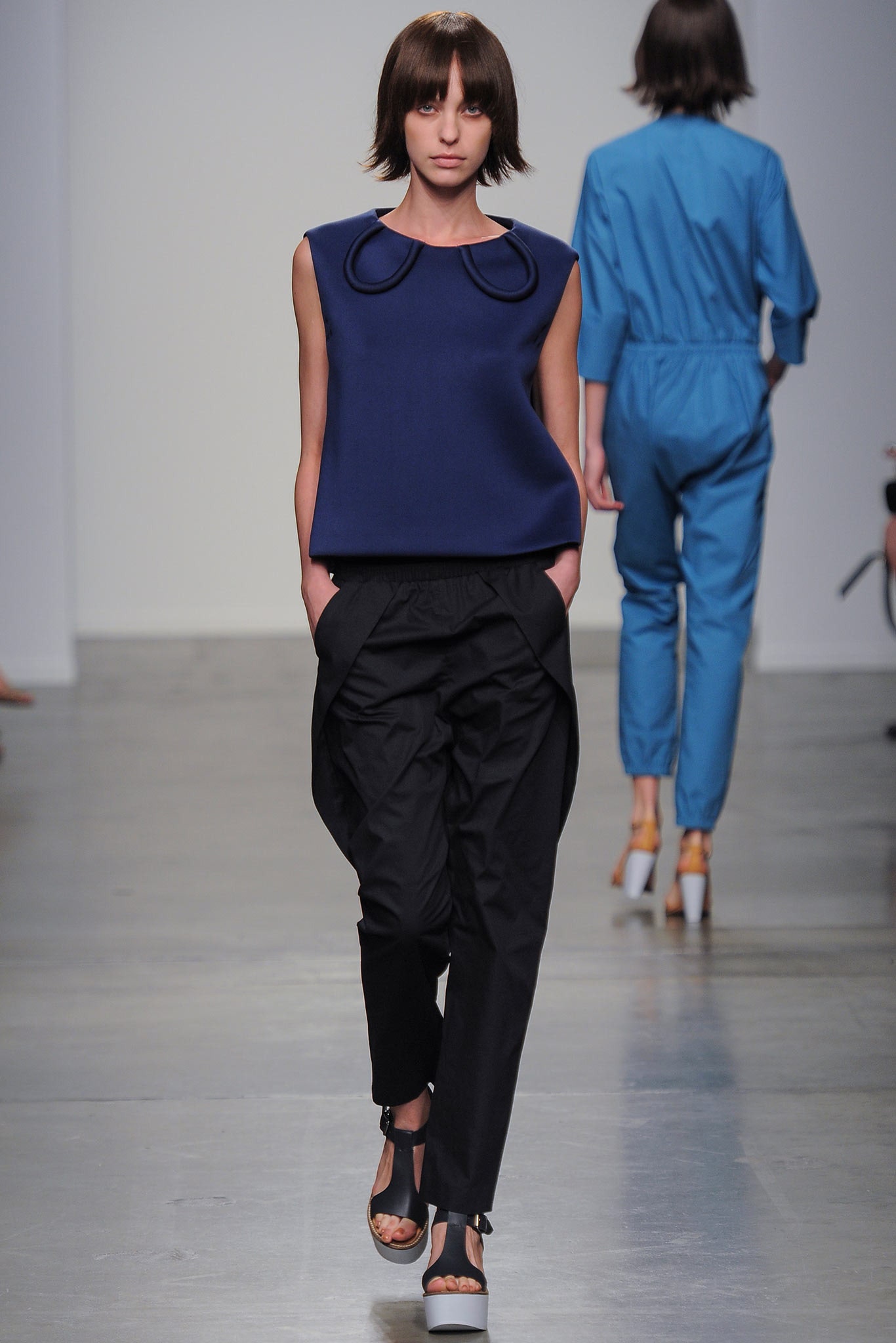 A relaxed blue sleeveless top with a collared design paired with black pants featuring an asymmetric detail.