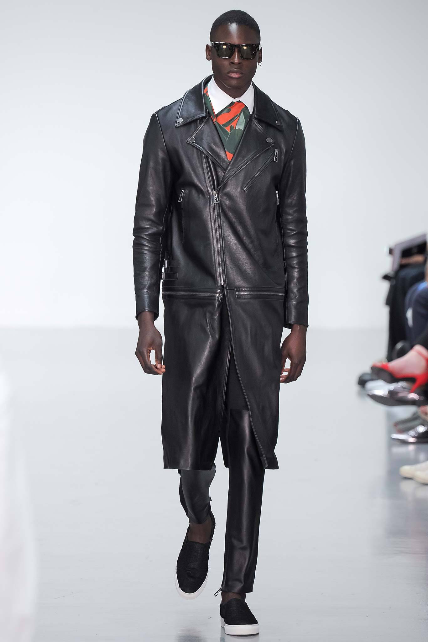 This black leather coat features a striking asymmetric design with zippered details, creating a bold silhouette. Paired with fitted pants, the ensemble exudes a modern edge, emphasizing sharp lines and a streamlined appearance.