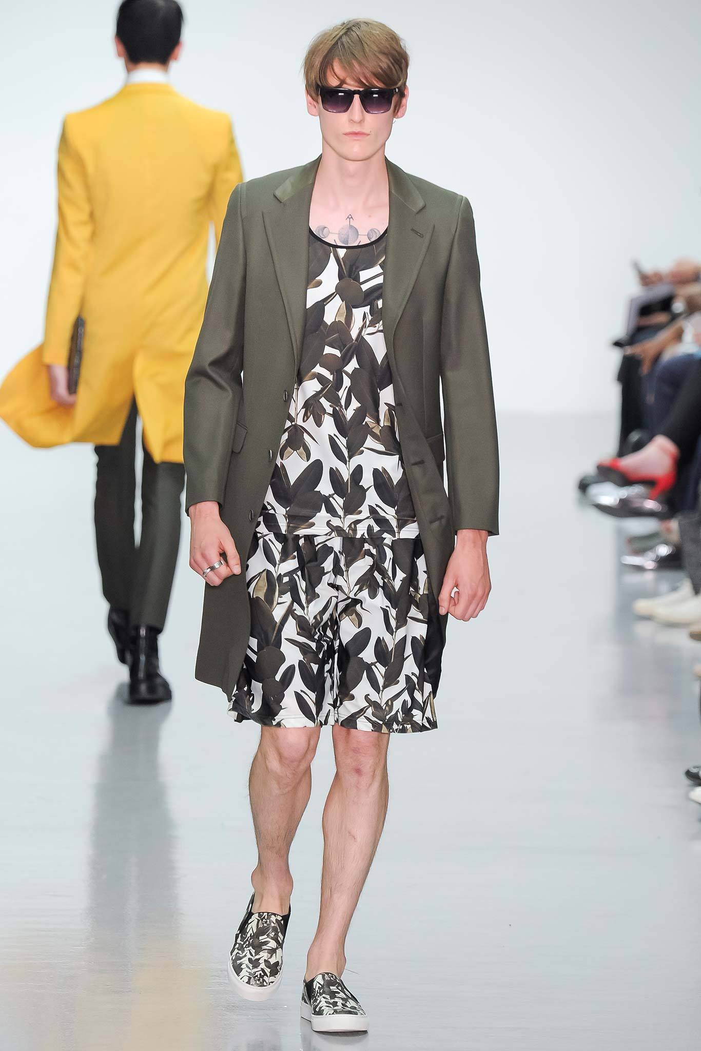 A relaxed jacket in a deep green hue layers effortlessly over a printed dress featuring a bold floral pattern. The long sleeves and collared design of the jacket complement the asymmetric cut of the dress, creating a dynamic interplay of shapes and textures.