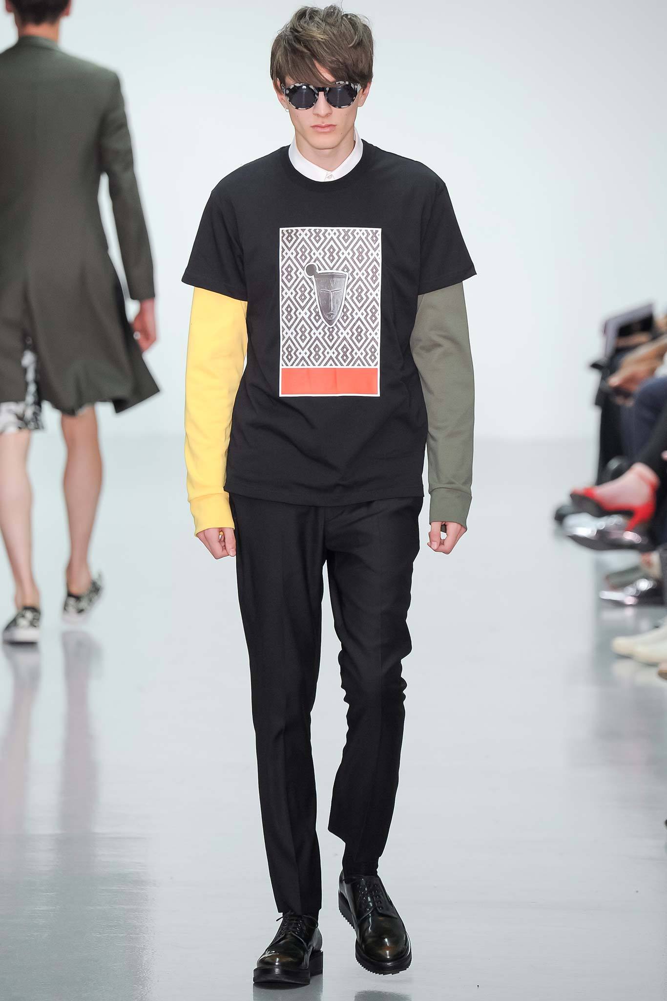 This ensemble features a relaxed black t-shirt adorned with a striking print, layered with long sleeves in contrasting colors. Paired with tailored pants, the look balances casual comfort with an artistic flair, creating a modern silhouette that captures attention.