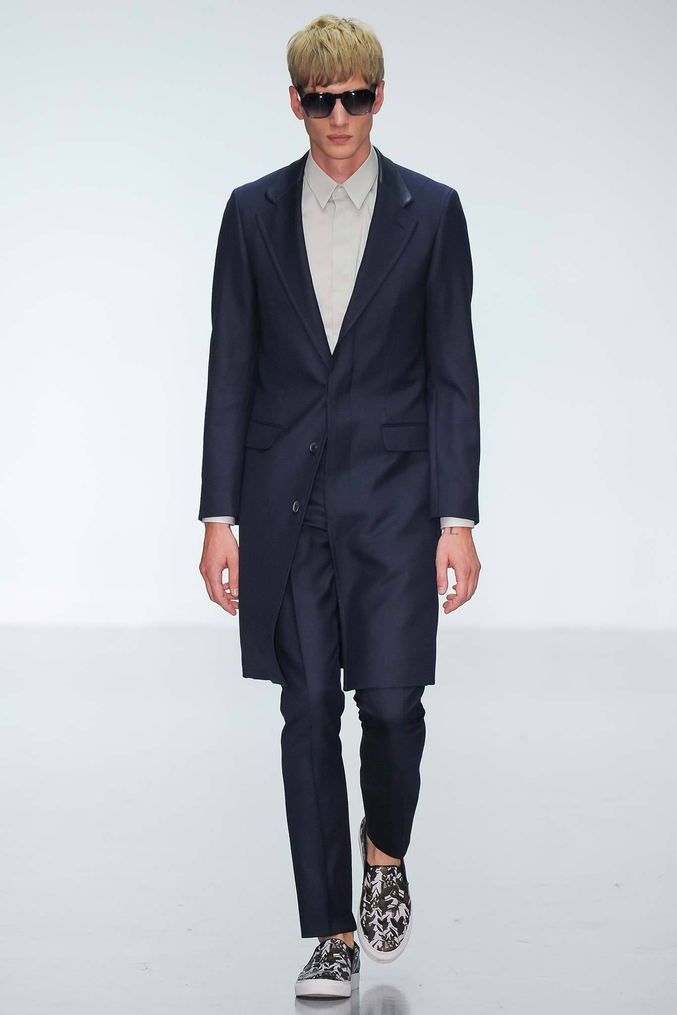 This tailored coat in a deep blue hue features a structured silhouette with a classic collared design, complemented by matching pants for a cohesive look. The buttoned front adds a touch of sophistication, while the overall ensemble exudes a modern, streamlined aesthetic.