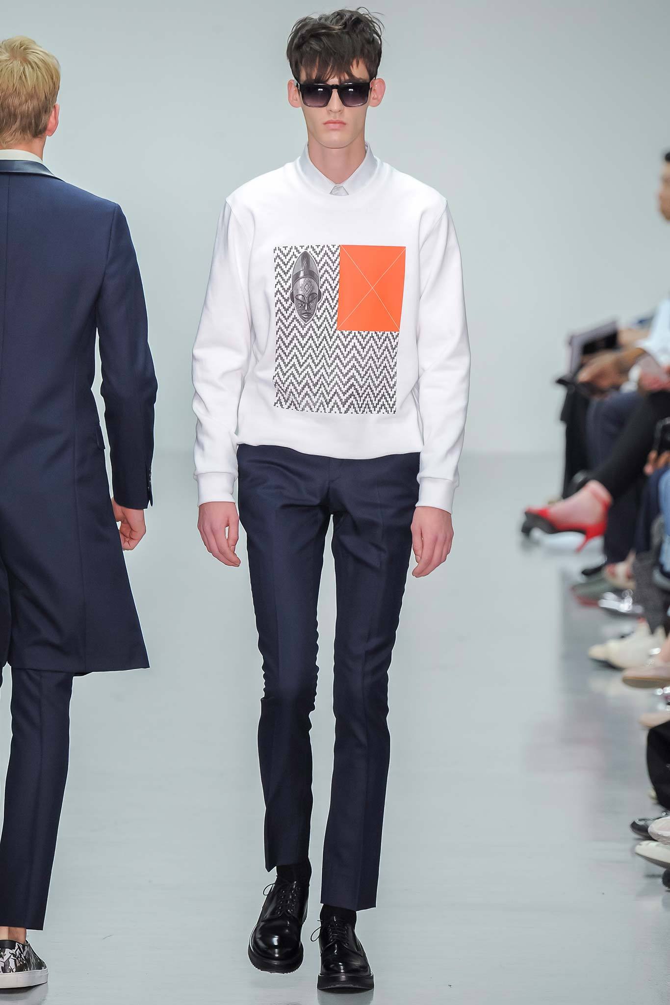 This ensemble features a fitted white sweater adorned with a striking graphic print, paired with slim blue pants that enhance the overall silhouette. The long sleeves and collared design add a touch of sophistication, while the contrasting elements create a dynamic visual interest.