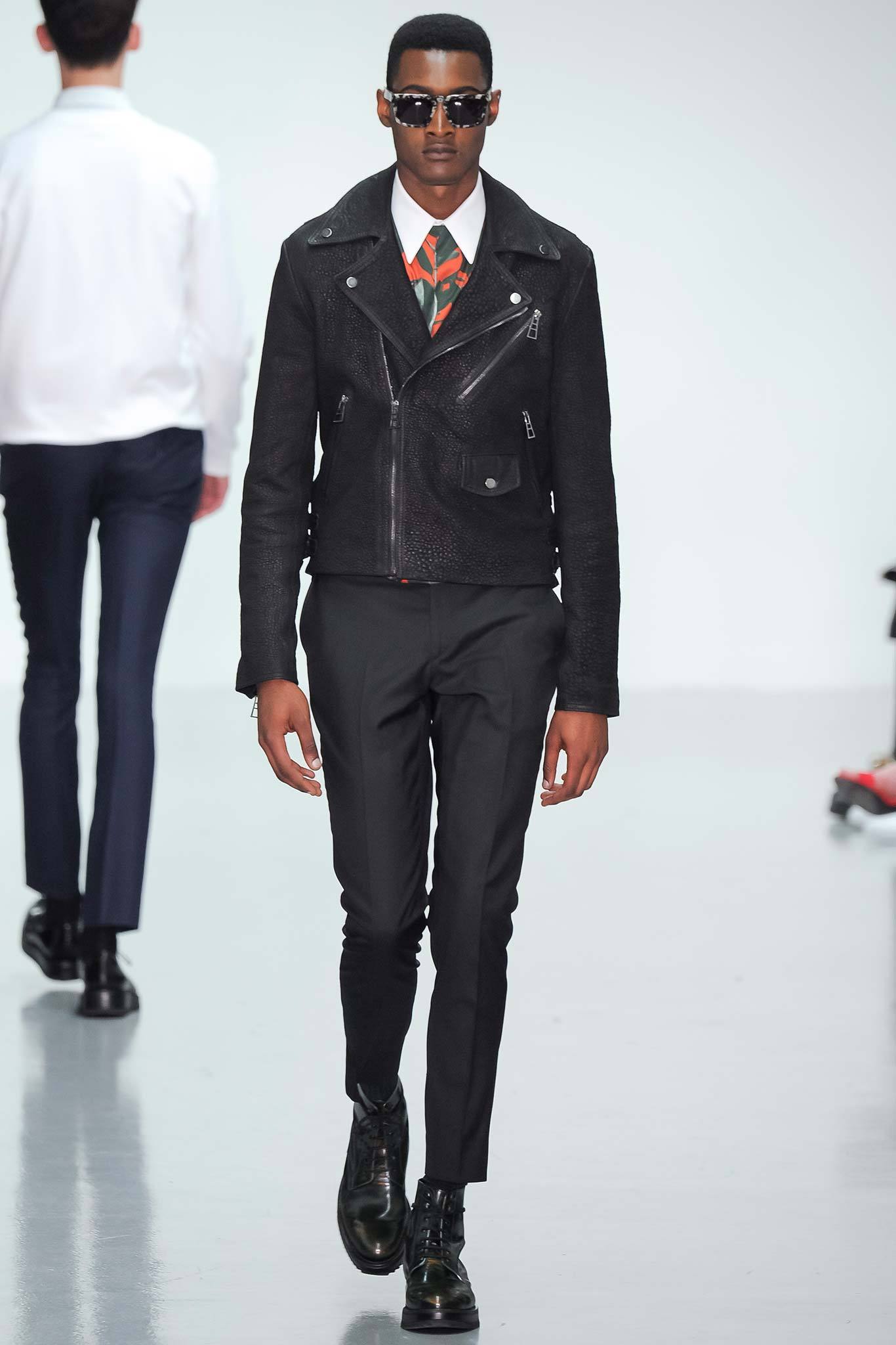 This fitted black leather jacket features a structured silhouette with a distinctive zippered closure, exuding a sense of modern edge. The long sleeves and collared design enhance its tailored appearance, making it a striking statement piece that pairs seamlessly with slim-fit pants.