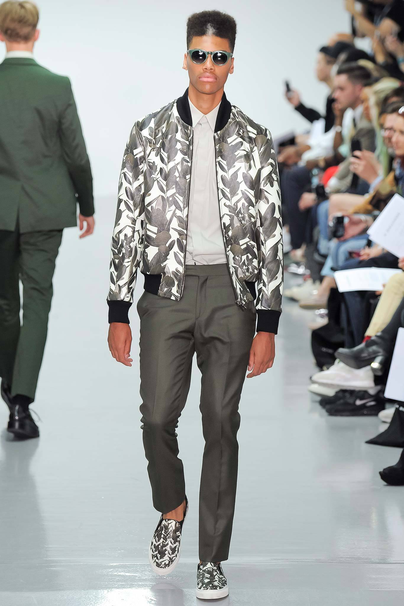 This ensemble features a fitted bomber jacket adorned with a striking floral print, complemented by tailored pants that enhance the overall silhouette. The combination of textures and patterns creates a dynamic visual interest, while the structured fit ensures a modern and polished appearance.