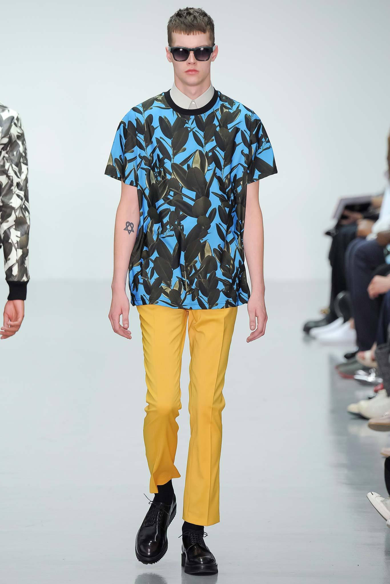 This relaxed t-shirt features a vibrant blue print that captures attention with its abstract design. Paired with yellow pants, the ensemble creates a striking contrast, emphasizing a playful yet contemporary aesthetic.