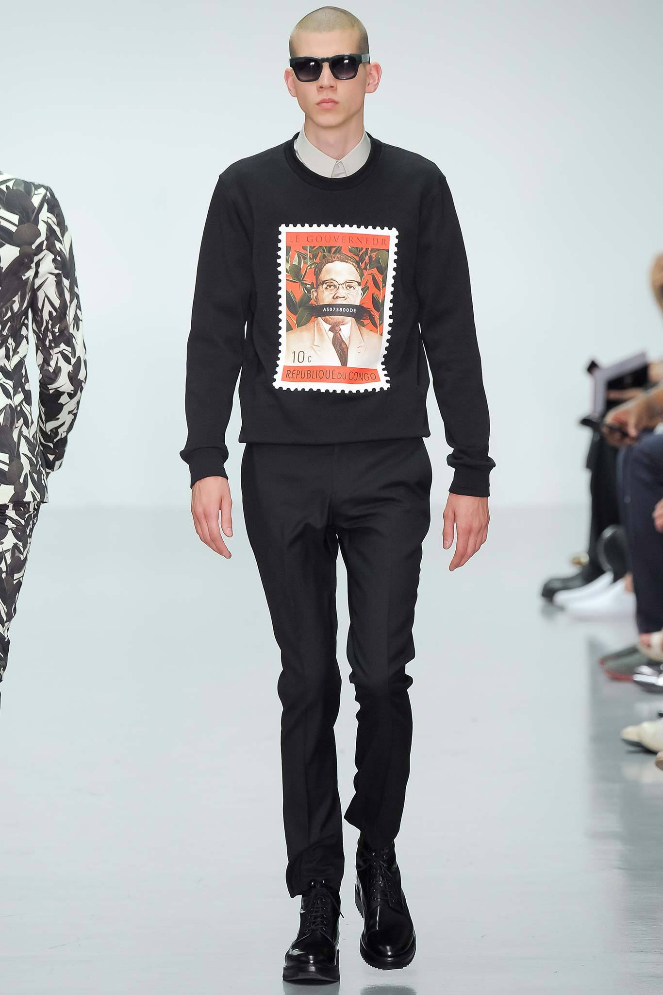 This ensemble features a fitted black sweater adorned with a striking graphic print, complemented by tailored black pants. The crew-neck design adds a casual touch, while the overall silhouette maintains a sleek and modern aesthetic.