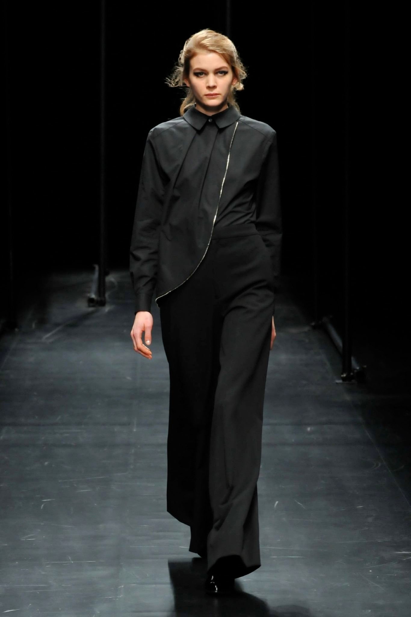 A fitted black jumpsuit with long sleeves, a collared neckline, and an asymmetric design.