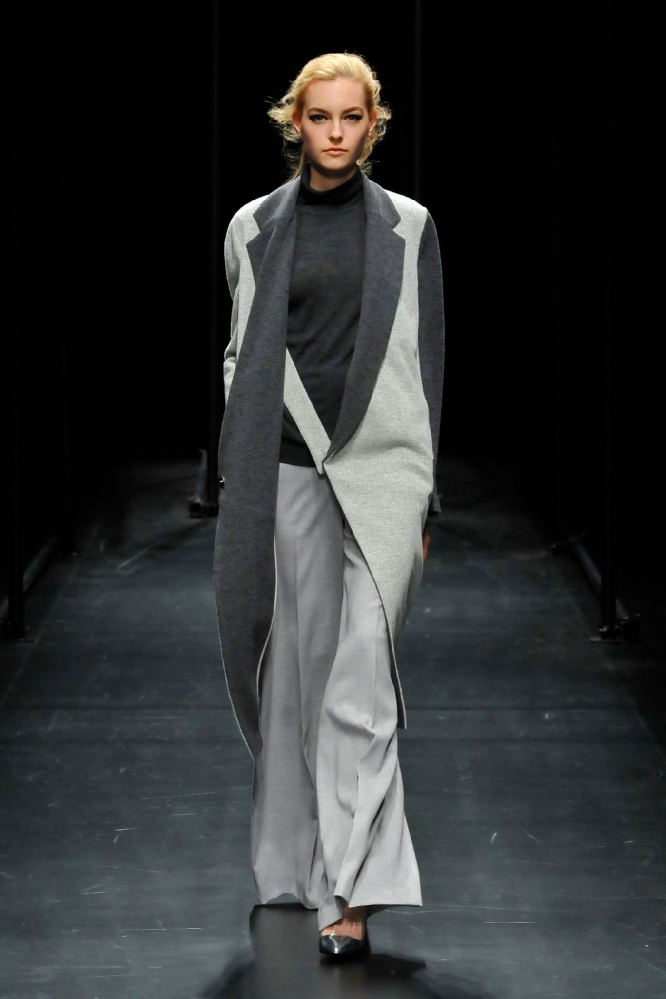 A relaxed gray wool coat with an asymmetric design paired with black pants.