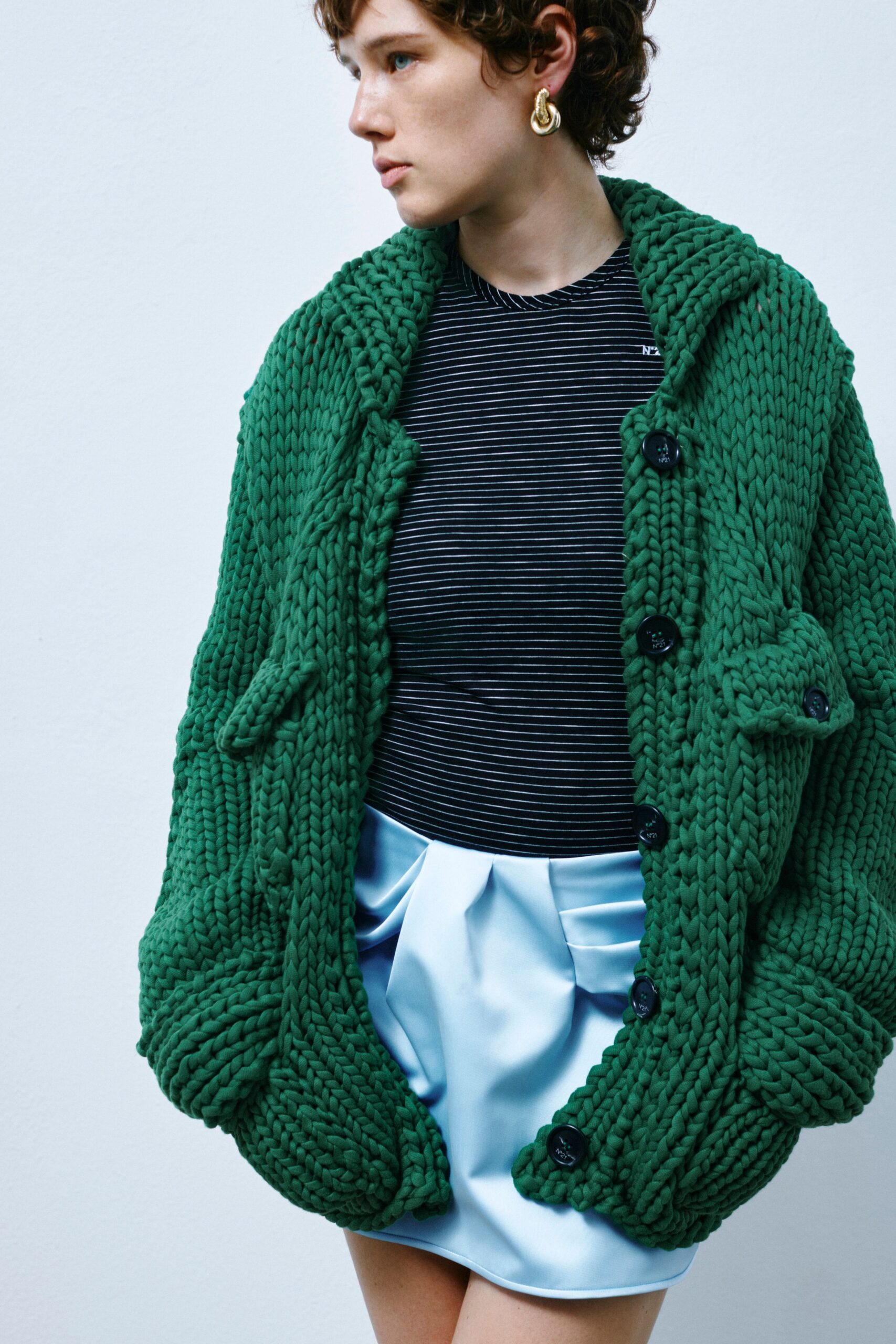 green oversized knitted coat with black striped top and blue pleated skirt
