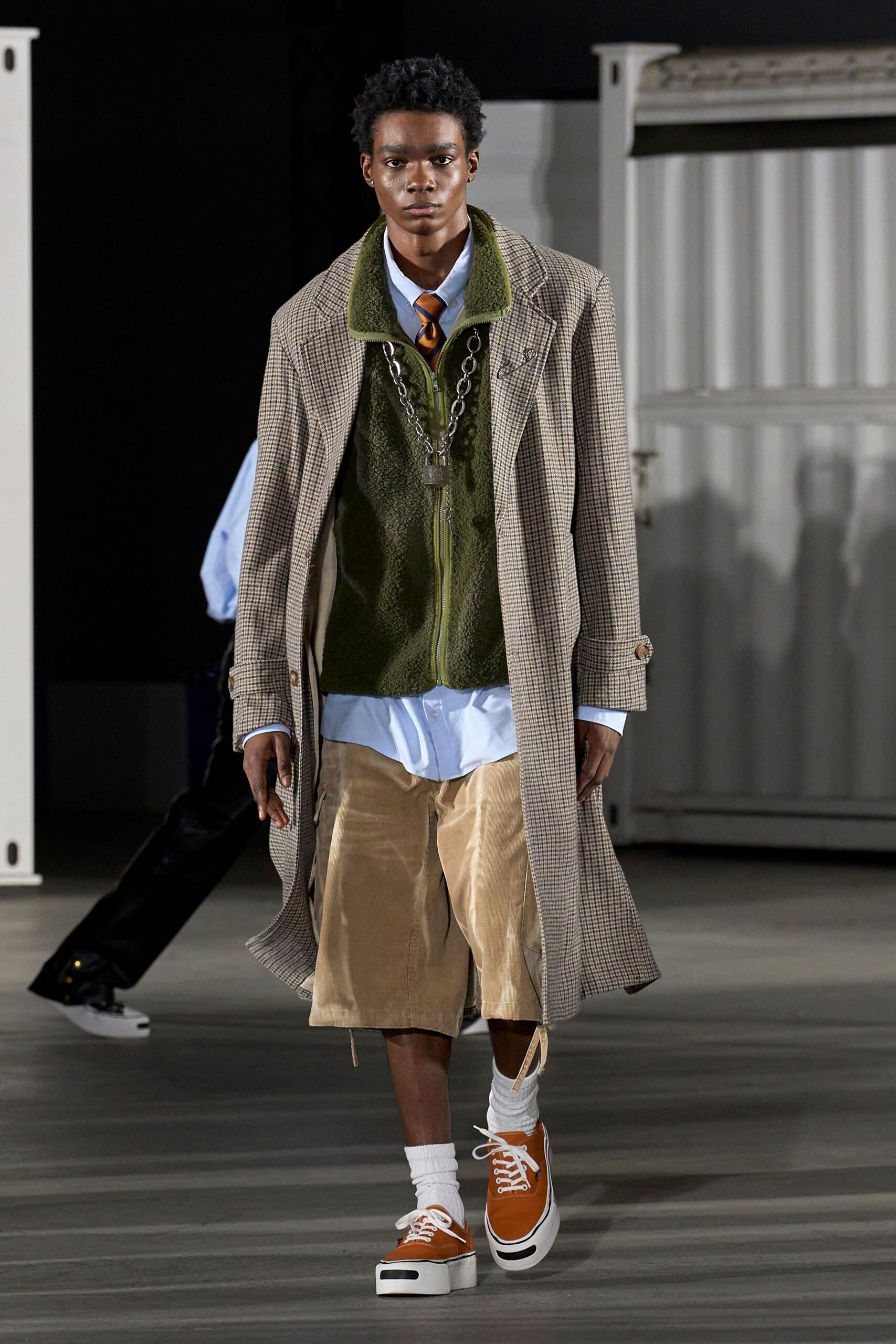 beige coat green vest blue shirt beige shorts orange shoes