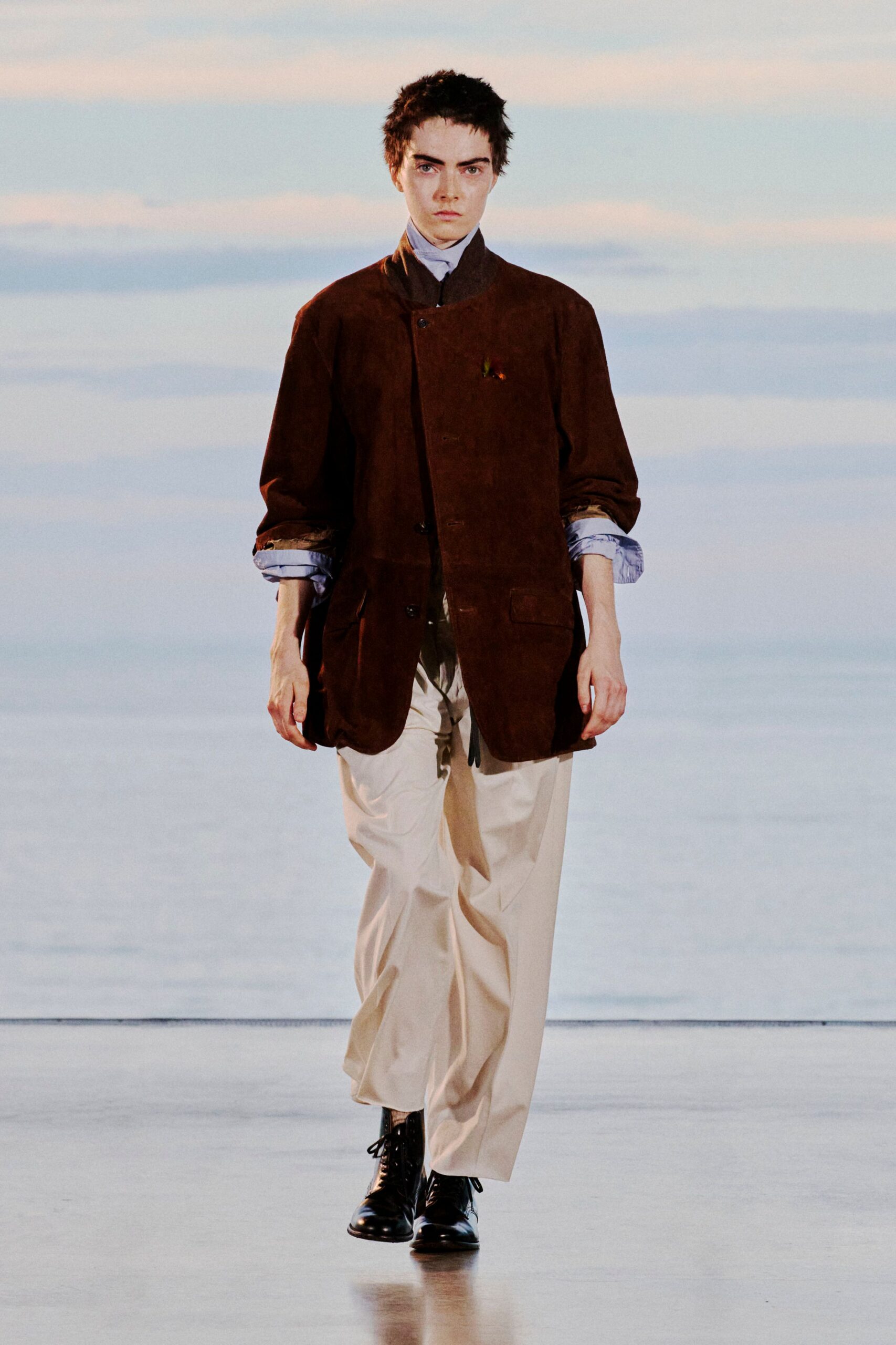Chocolate suede jacket with a stand collar and pale blue poplin cuffs rolled back. Dark tie over a high pale shirt, cream trousers with a loose break, black leather lace-up boots. Like stepping out just before the ferry horn.