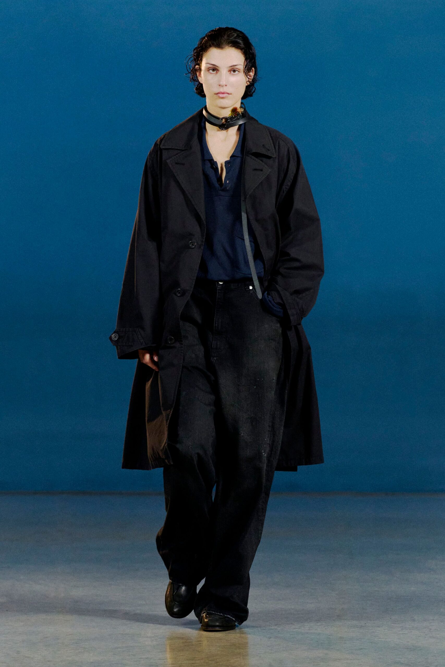 Black trench coat in crisp cotton twill, sleeves cinched with tab cuffs. Deep navy placket shirt with a raw notch at the neck, washed black jeans, square-toe leather shoes. Like stepping out for cigarettes after the last train.
