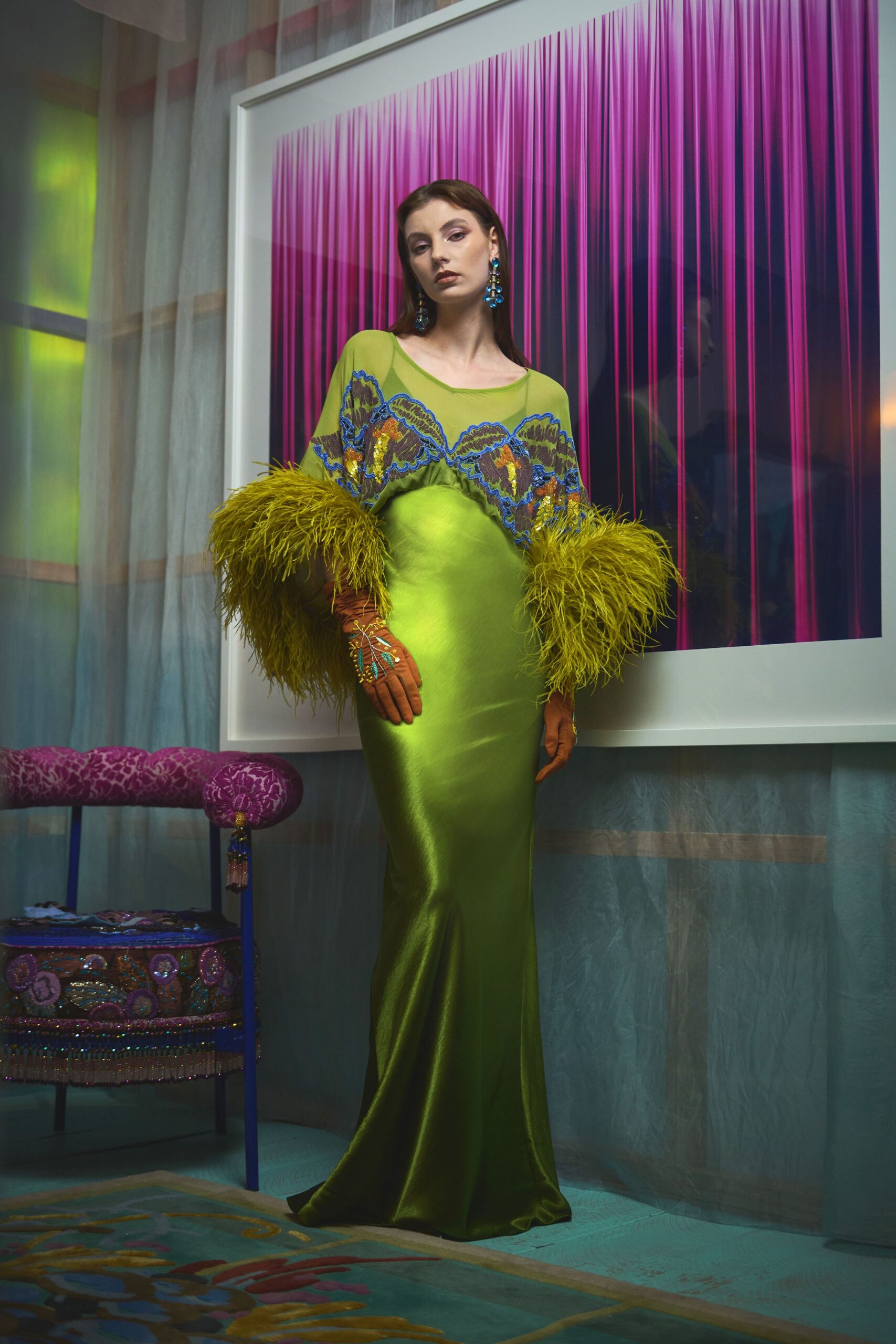 Lime satin column gown with a sheer mesh yoke, blue-edged sequin appliqué and ostrich-feather cuffs brushing the hips. Rust gloves beaded with tiny sprigs, cobalt drop earrings. Waiting by the hotel suite art before midnight champagne.