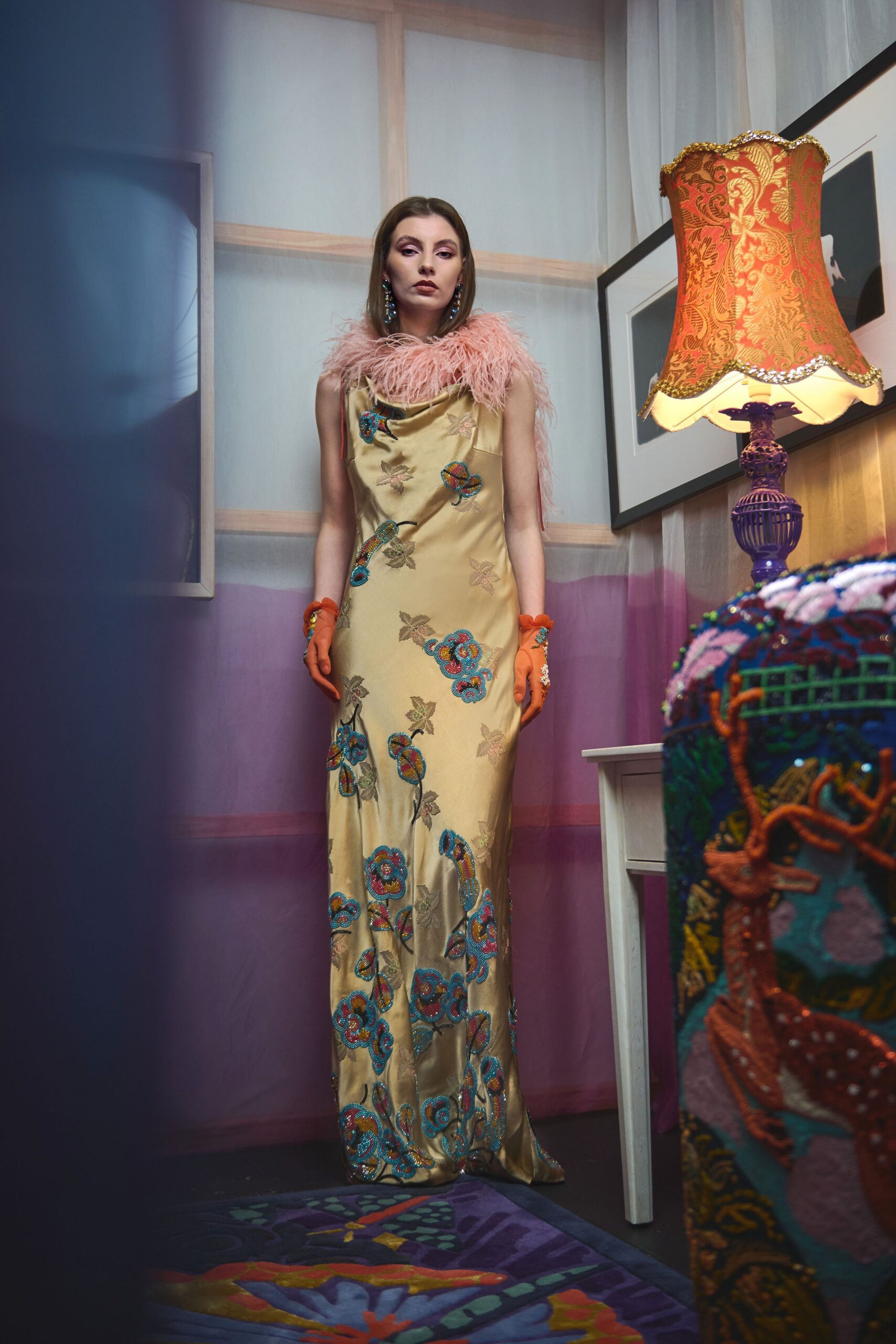 Champagne satin column dress scattered with turquoise bead-embroidered flowers, topped with a blush ostrich-feather stole. Orange mesh gloves with jeweled cuffs. Waiting beside a fringed lampshade after midnight.