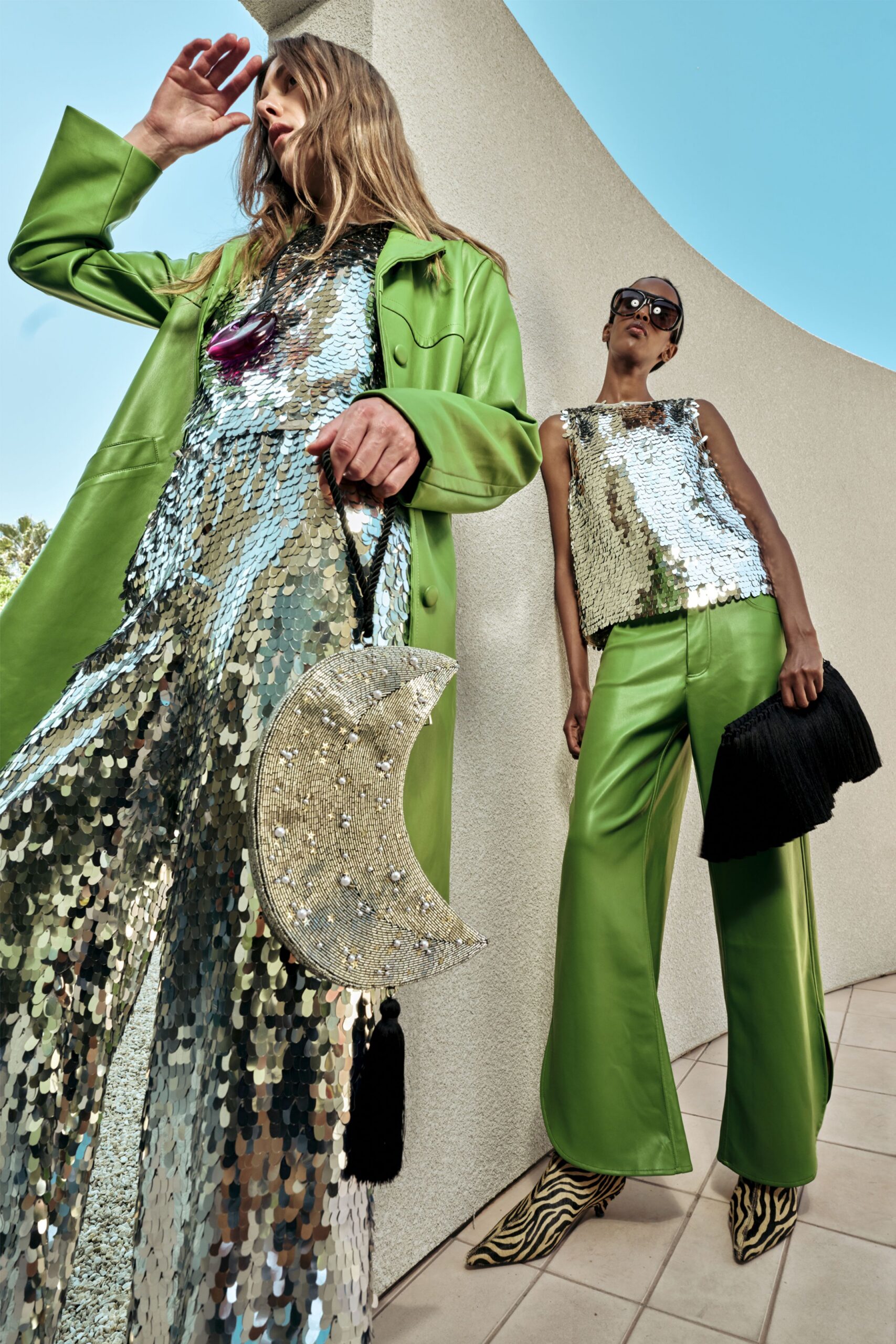 Silver paillette column dress under a lime leather coat with wide turned-back cuffs, a plum resin pendant at the chest. Crescent beaded bag dotted with pearls, black tassel swing. Sun glaring off concrete steps.