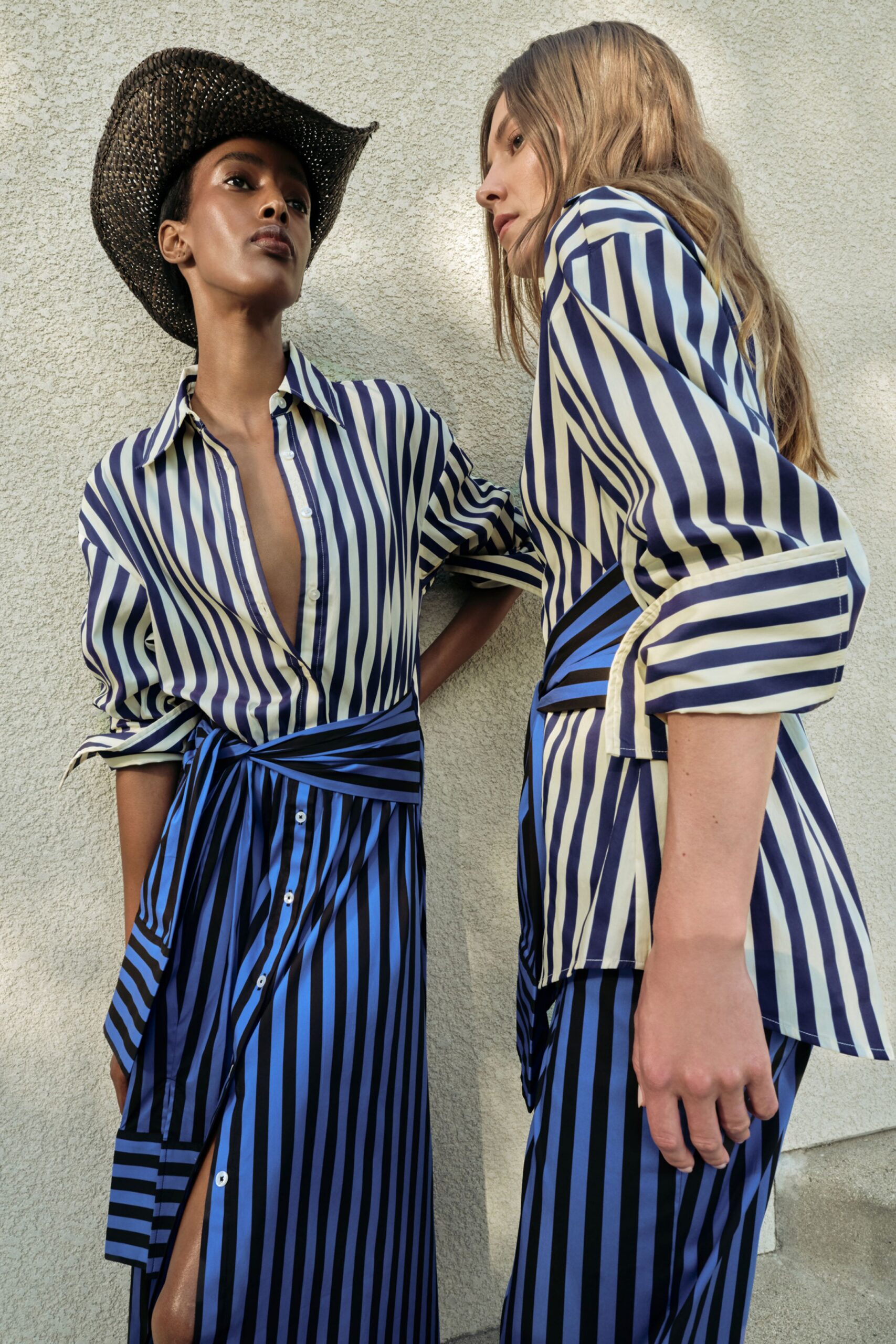 Blue-and-cream satin striped shirtdress, collar open to the sternum and sleeves turned back in broad cuffs. Twisted sash at the waist, button placket breaking into a thigh slit. Sun on stucco after a poolside lunch.