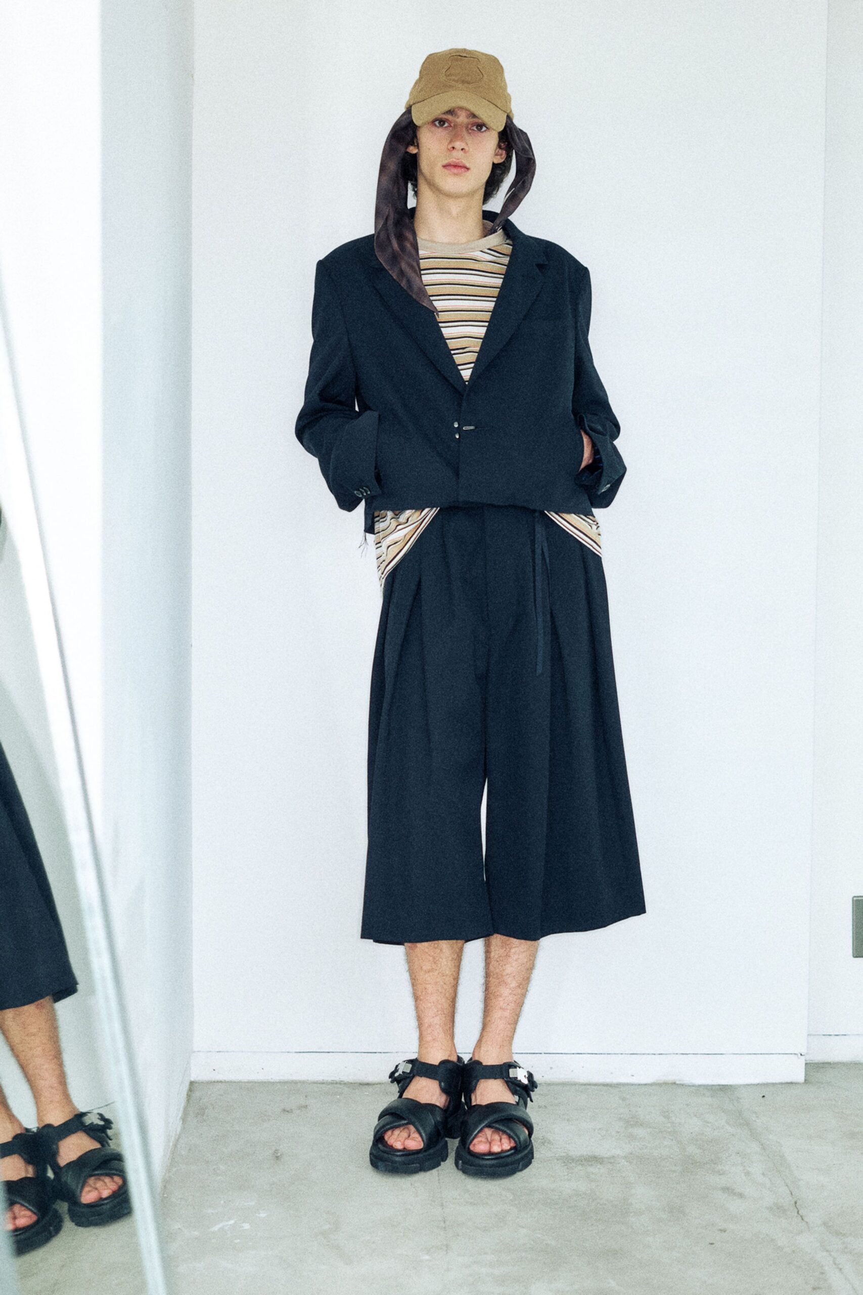 Sand cotton cap with long satin ear flaps, cropped black blazer with a low single fastening, cream-and-tan striped jersey tee, black culottes cut with deep front pleats, thick strapped sandals. Waiting by the freight lift on move-in day.