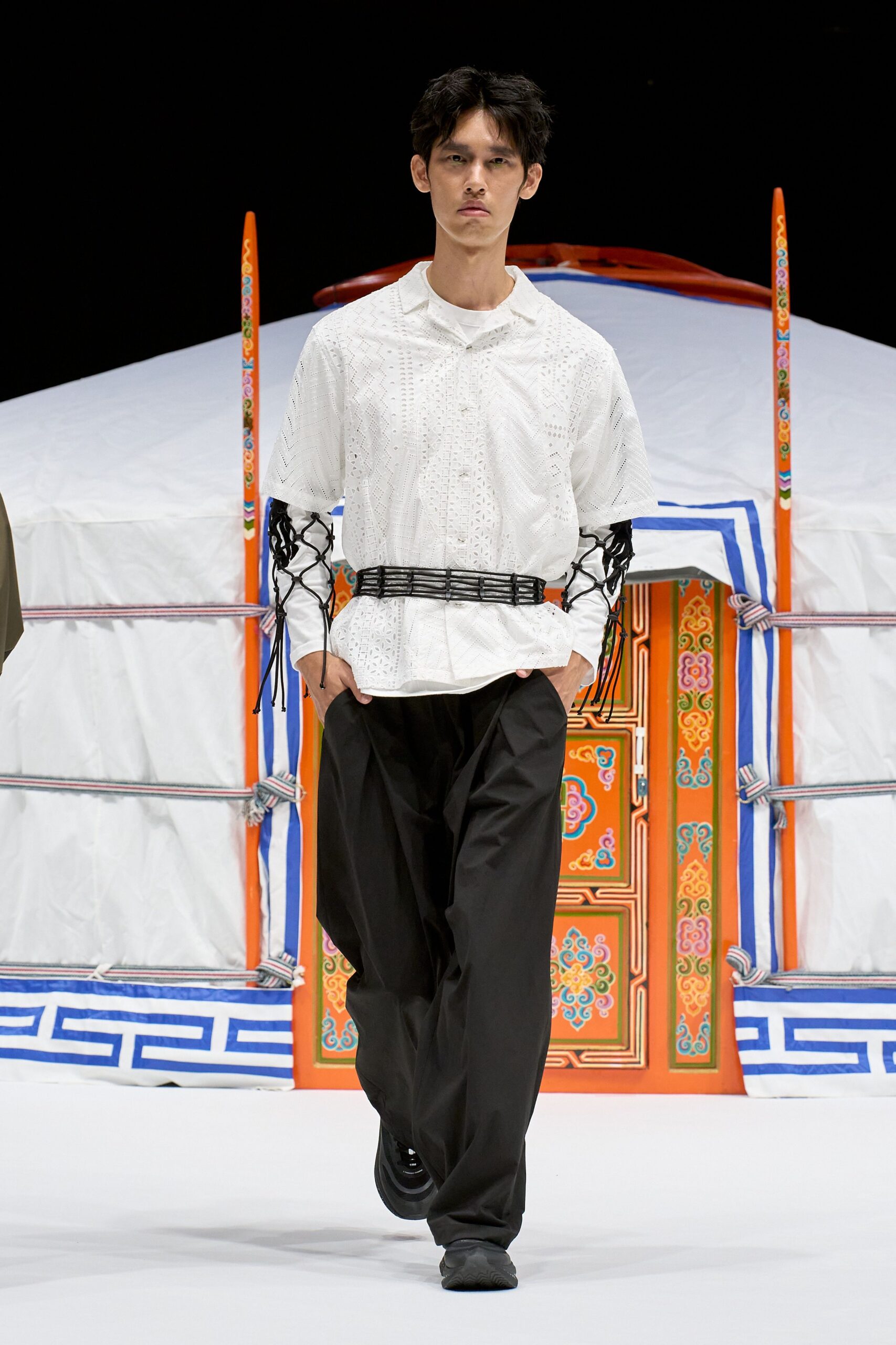 White eyelet camp-collar shirt cinched with a black lattice cord belt, white jersey long sleeves laced in open net at the arms, black poplin wide-leg trousers, black trainers. Like stepping out into cold air after a yurt dinner.