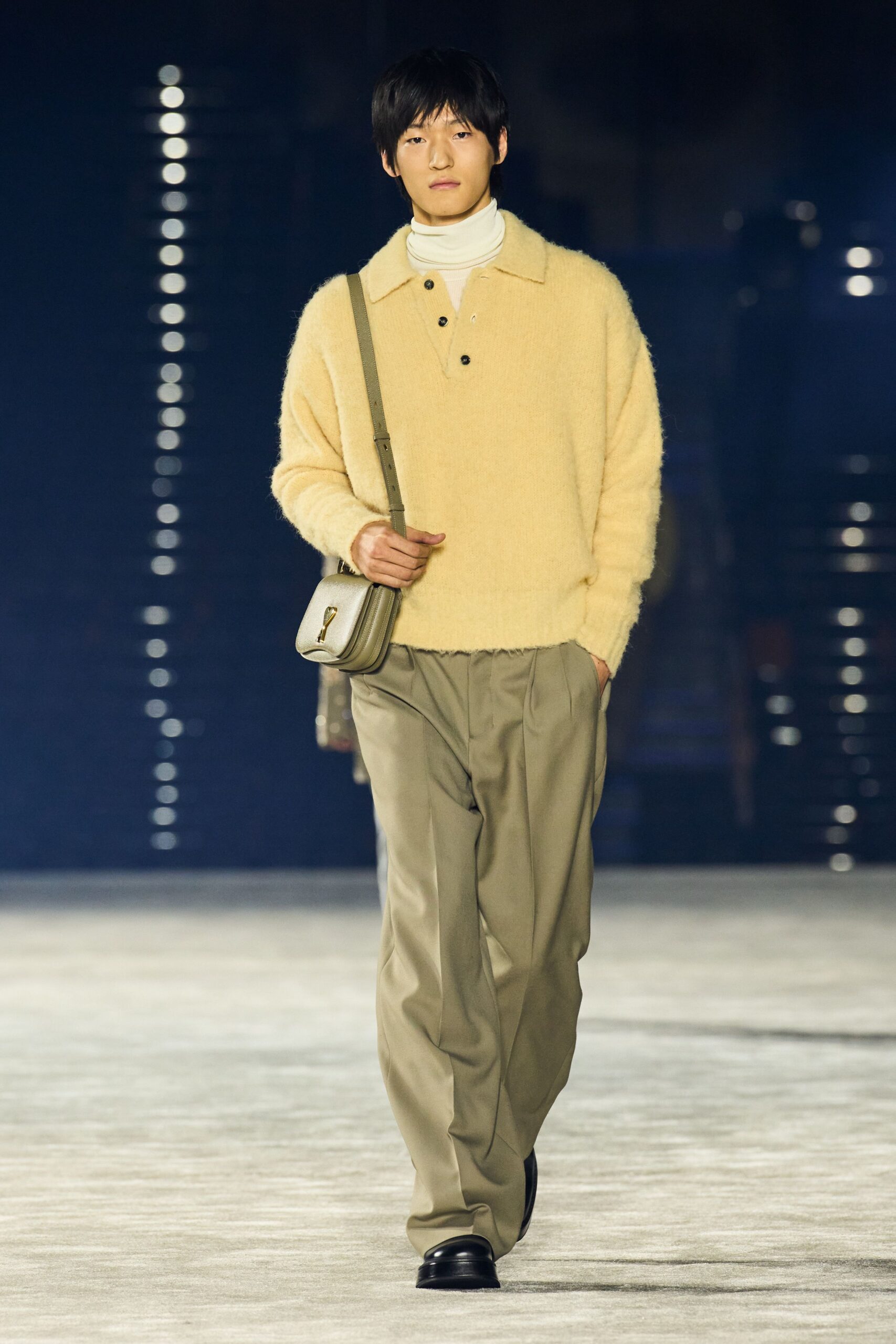 White jersey turtleneck, collar stacked close under the chin. Buttercream fuzzy-knit polo, black buttons dropping from the open placket. Pale grey leather box bag with a gold wedge clasp. Taupe pleated trousers falling long over the shoe. Black square-toe shoes. Early ferry crossing, coffee cooling between both hands.