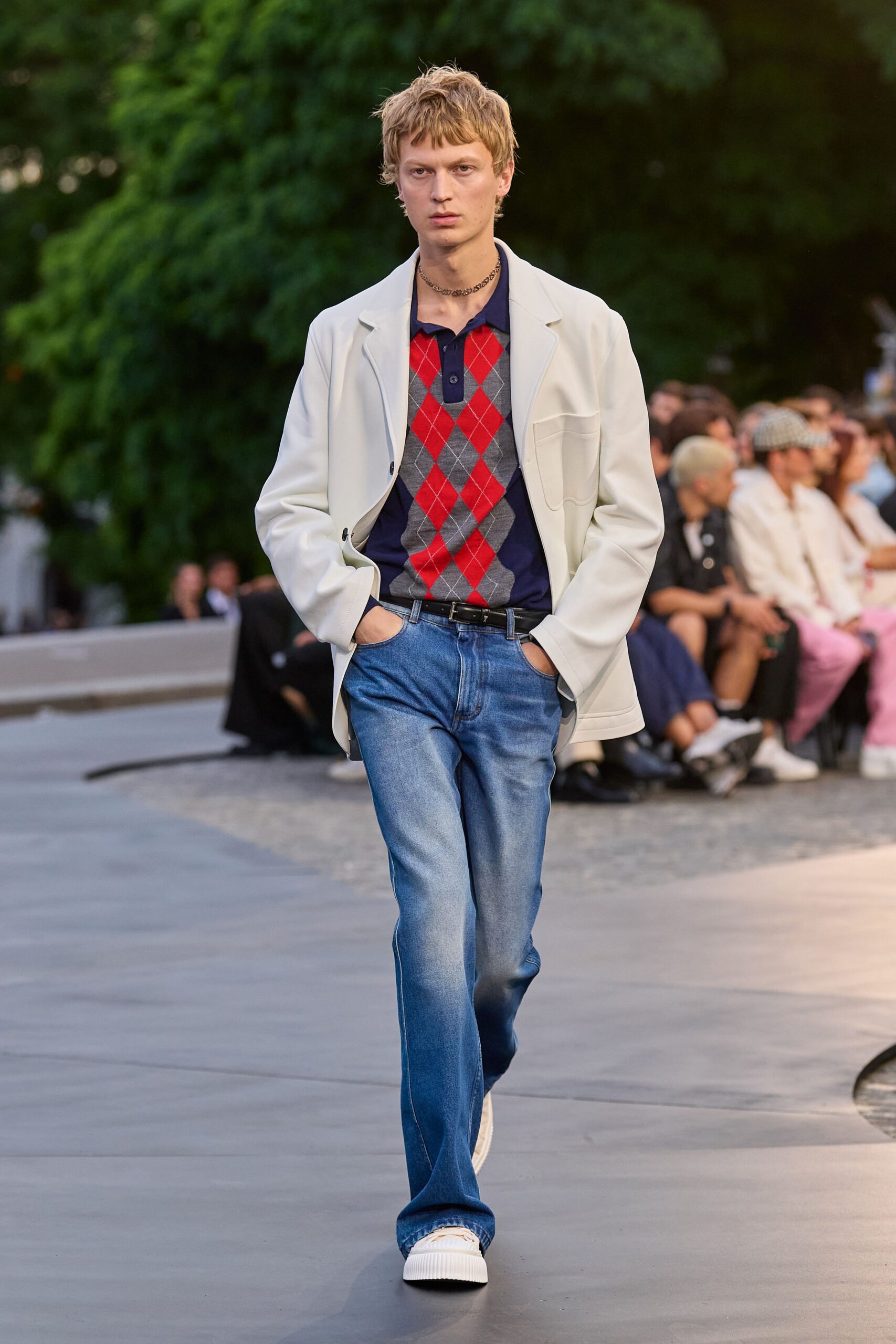 Chalk blazer in smooth bonded cloth, one low black button. Navy knit polo fronted with red and grey argyle. Mid-wash bootcut jeans, whiskered pale at the thighs. Slim black leather belt. Cream ribbed-sole sneakers. Crossing the lawn to a garden party that turned cooler after sunset.