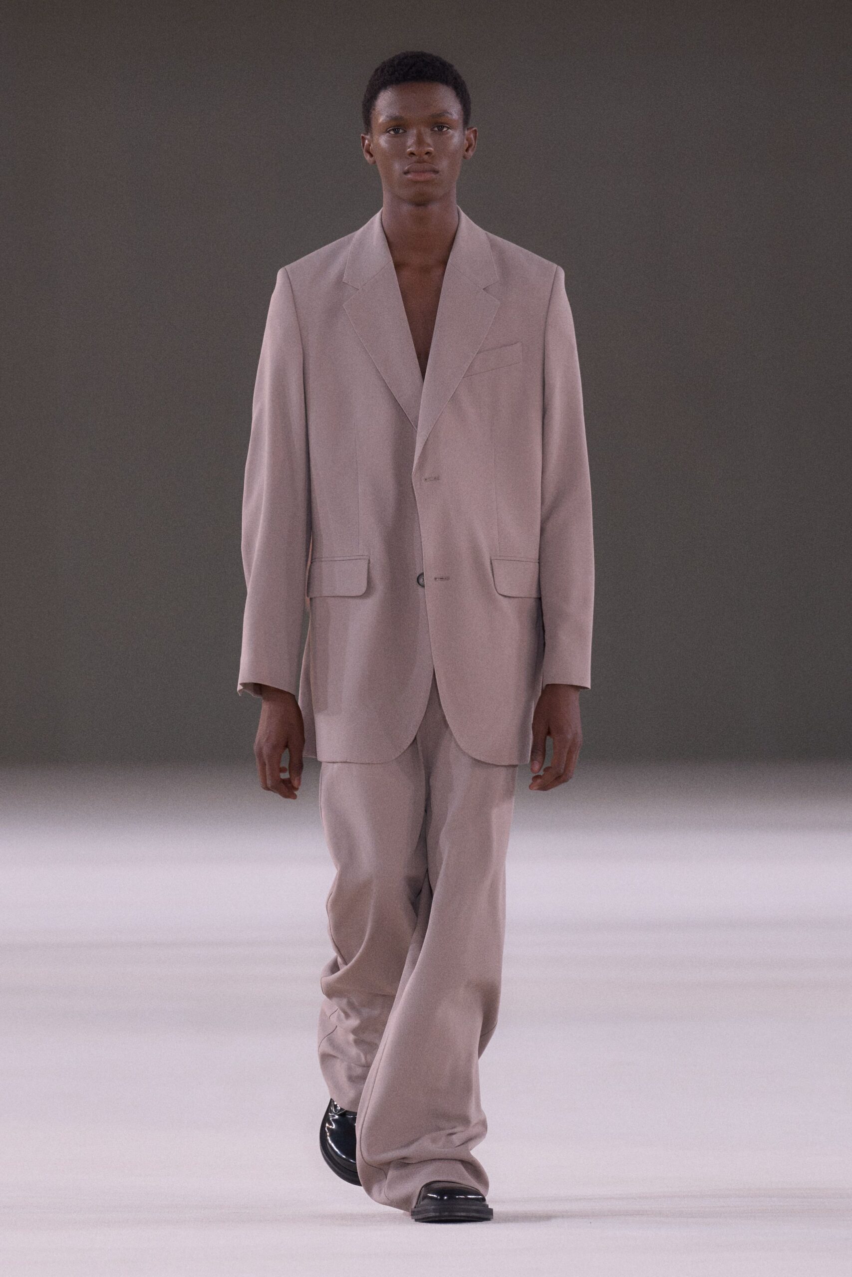 Dusty-mauve tailored blazer, dropped shoulders and a low two-button stance. Matching trousers pooling softly over the shoes in fluid suiting cloth. Black leather square toes with a hard mirror shine. Whatever you wear to collect keys for an empty apartment at dusk.
