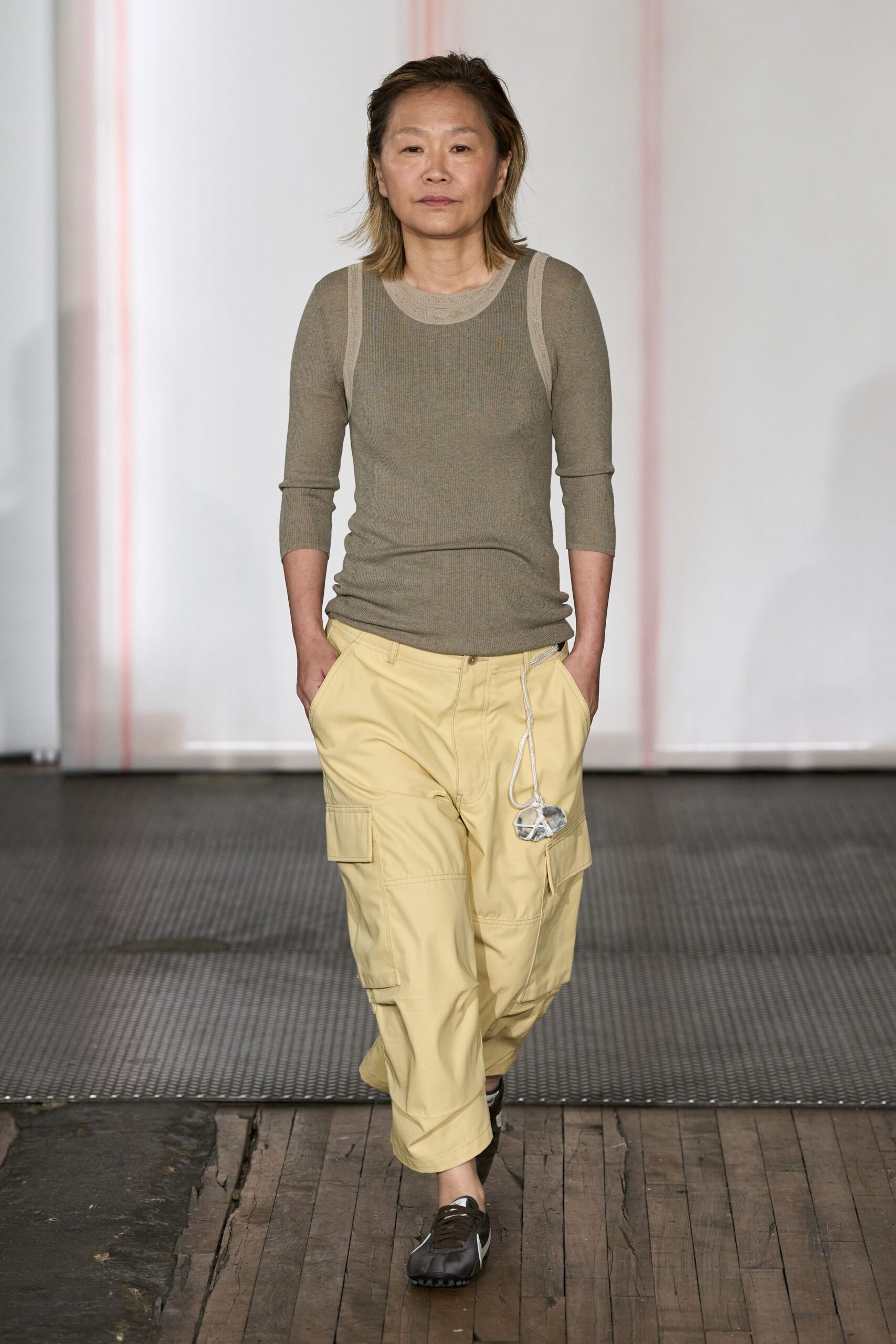 Sheer taupe ribbed knit top with pale binding tracing the armholes. Butter yellow cargo pants with panel seams and a rope drawcord dangling a small pouch. Brown track sneakers with a white side flash. Walking the long way home after buying fruit and hardware.
