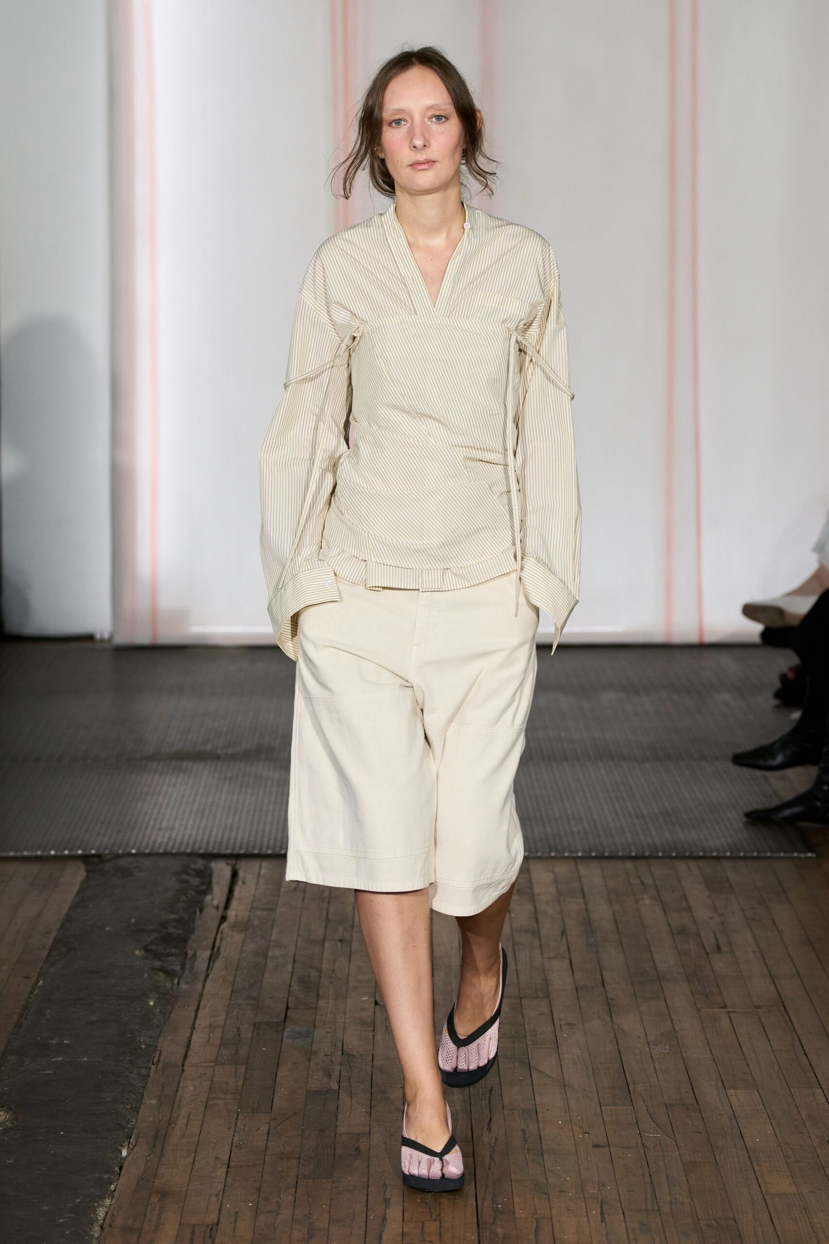 Cream pinstriped blouse, drawstrings cinching under the arms and along the side. Off-white knee-length shorts in sturdy twill with broad hem bands. Pink mesh thong heels with black binding. Walking across old floorboards to borrow milk from the downstairs neighbor.