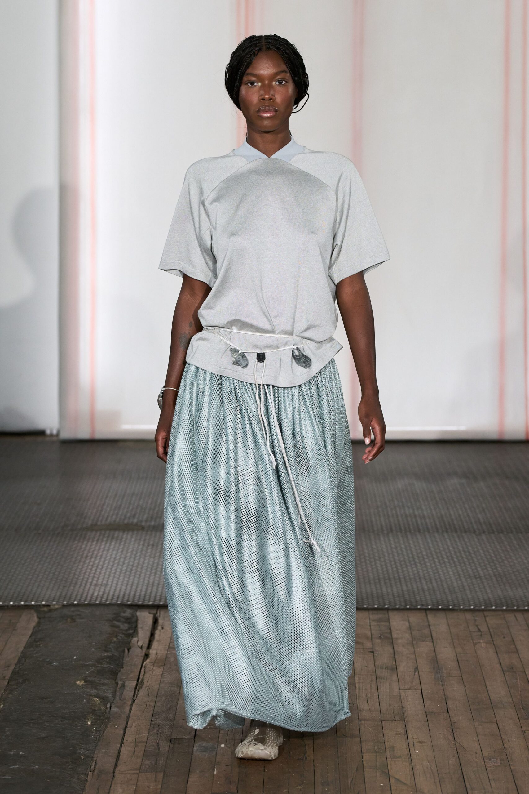 Pale grey jersey top with a crossover collar and peplum drawcord hem. Ice-blue open mesh maxi skirt, softly gathered into the waist. Marbled grey flats peeking from the pooled hem. Walking across warped floorboards after the hall has finally emptied.