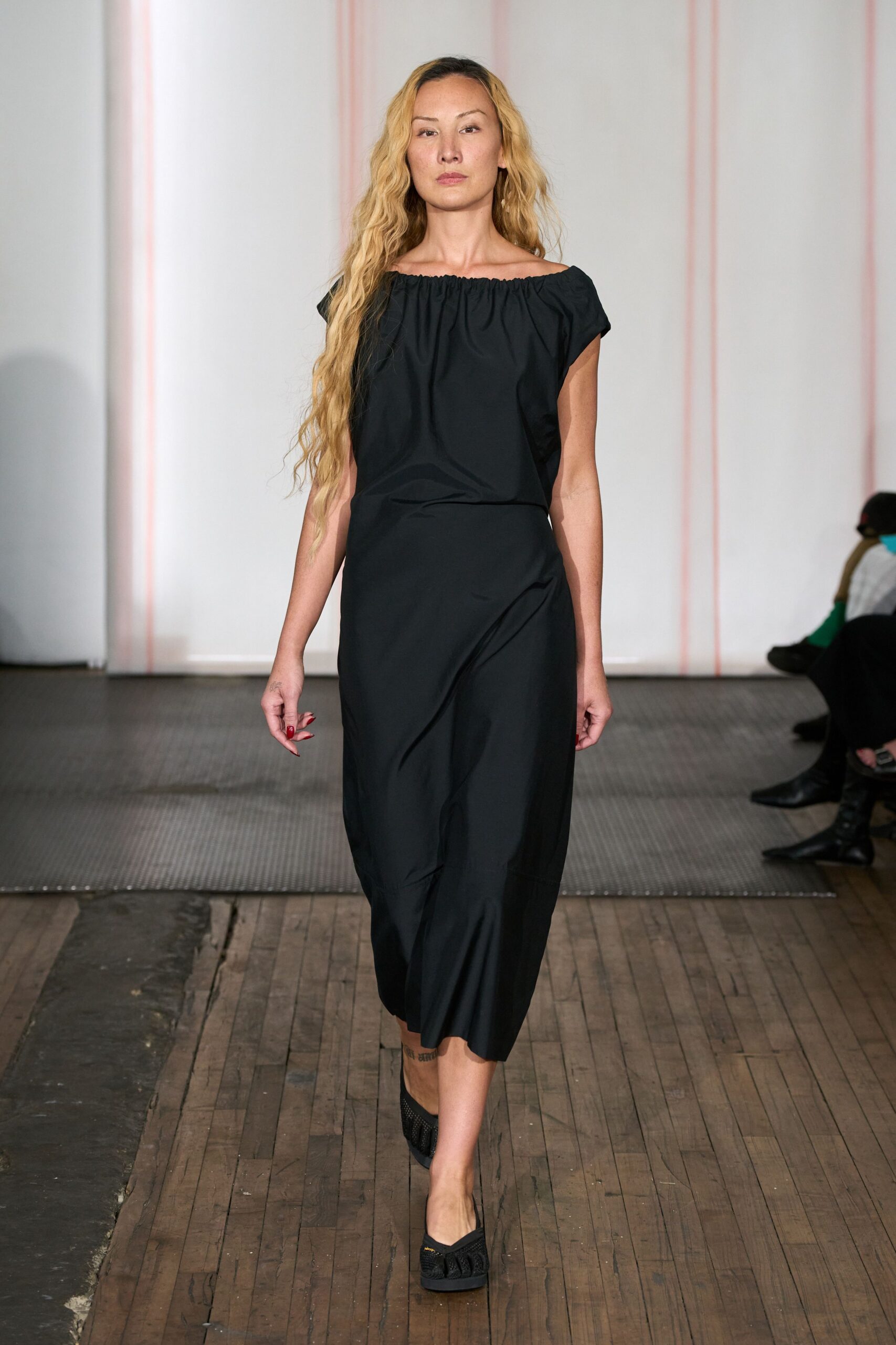 Black poplin dress with an elastic boat neckline and twisted draped skirt. Black mesh flats with a braided strap across the vamp. Crossing a drafty town hall after the wedding chairs are stacked.
