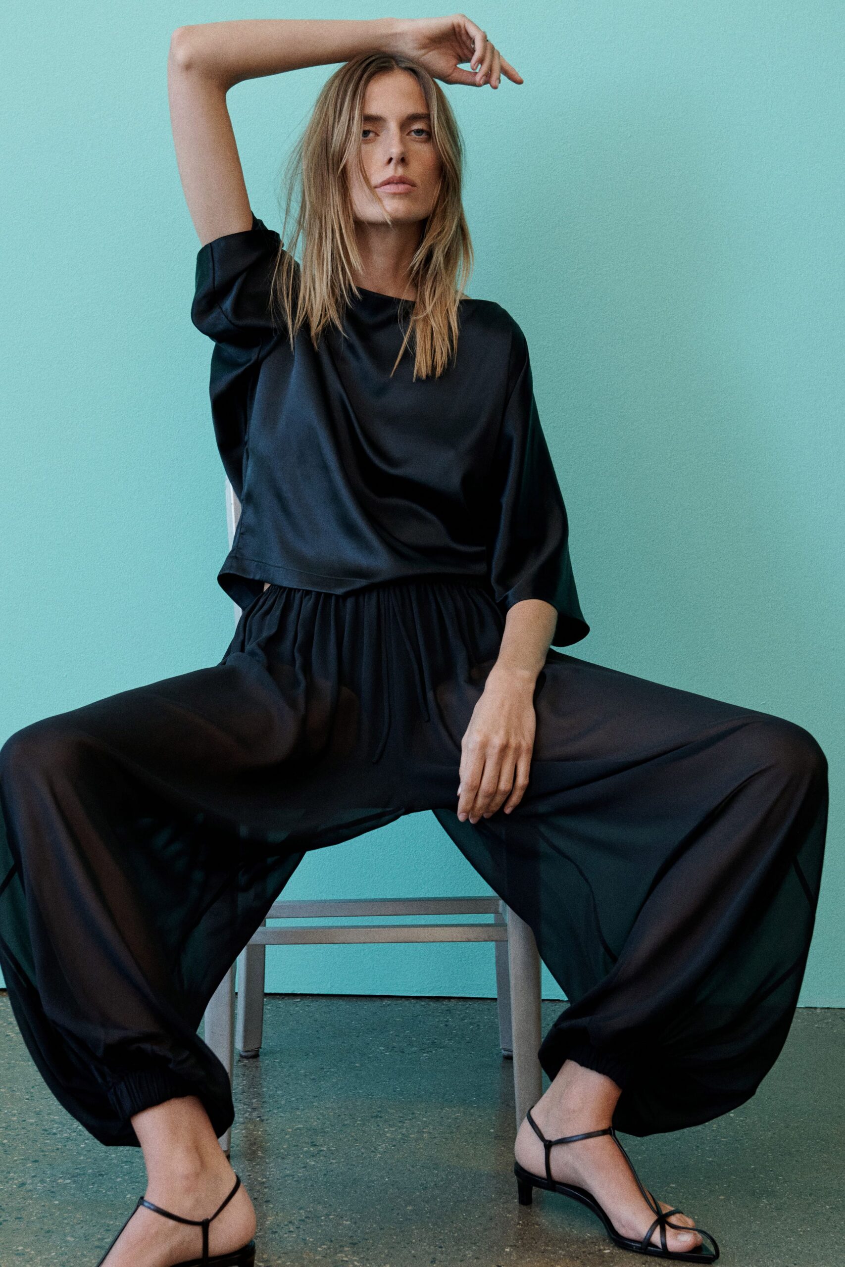 Black satin blouse with a wide bateau neck and dropped sleeves. Billowing black silk trousers, drawstring waist gathered into snug ankle cuffs. Barely there black leather thong sandals on a low heel. Sitting through a heatwave dinner with all the windows open.