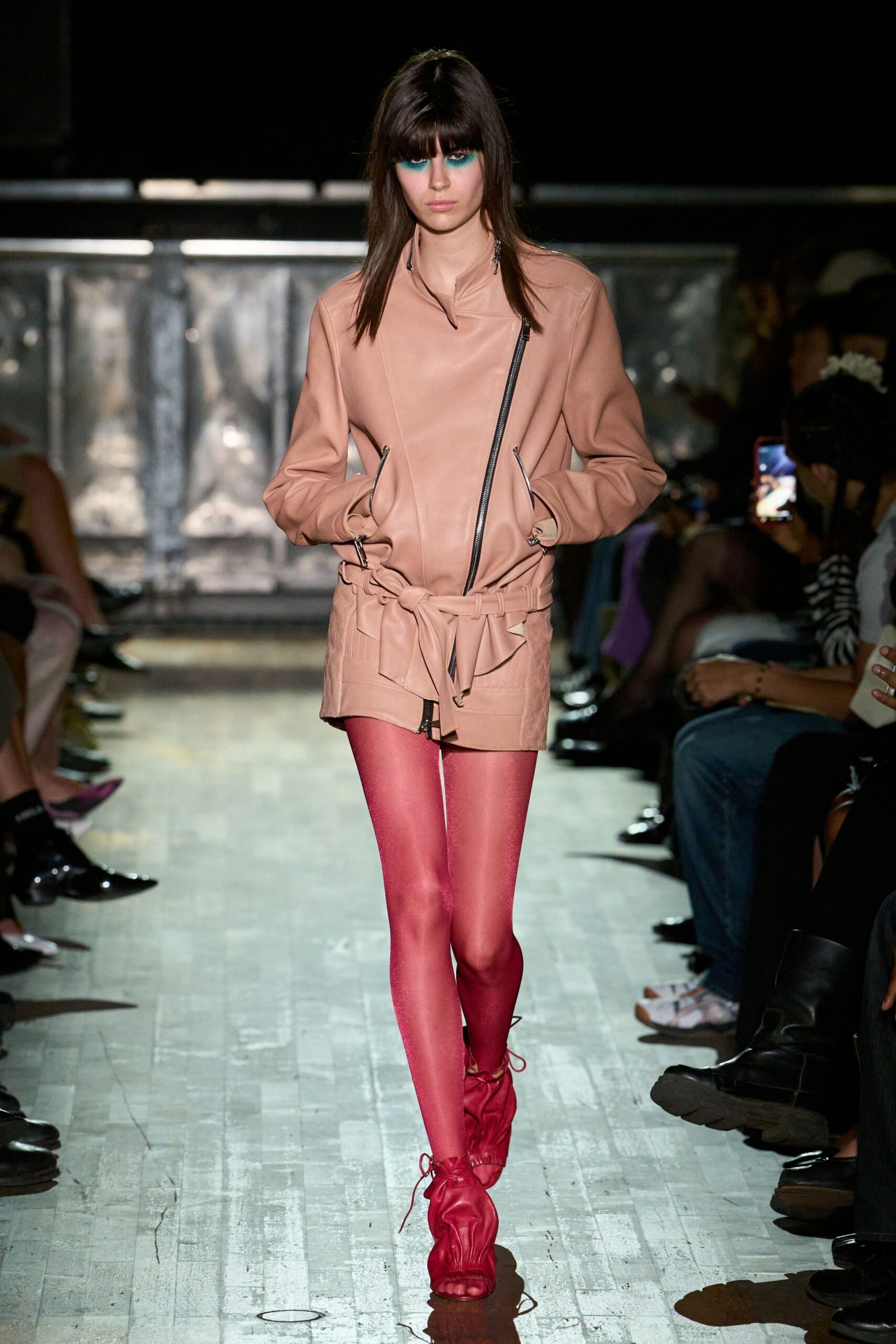 Blush leather biker jacket with an off-center zip and self belt. Sheer fuchsia tights catching the light with a faint shimmer. Red leather sandals ruched over the foot, laces winding the ankle. Walking across a gym floor after the school dance emptied out.