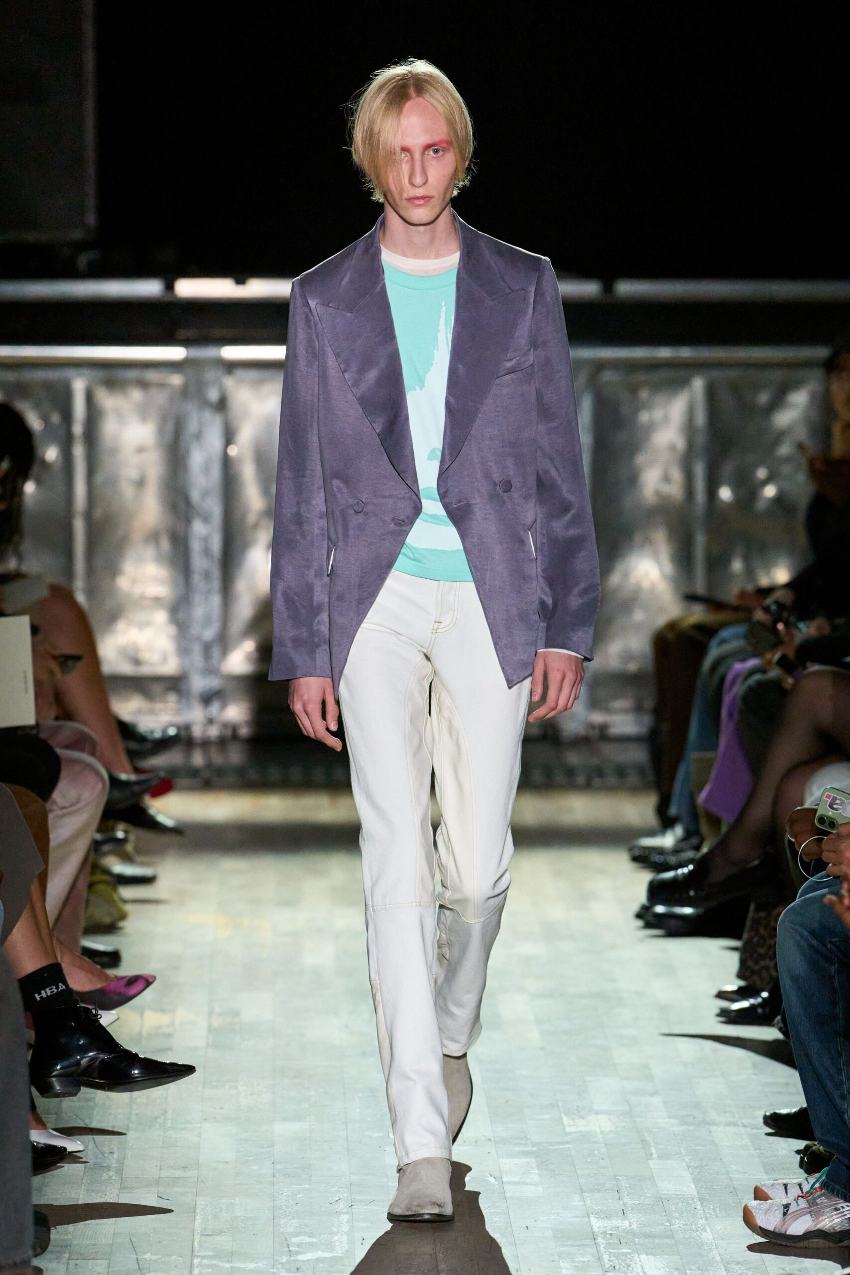 Dusty violet satin blazer with exaggerated peak lapels and slanted welt pockets. Aqua tee washed with a pale white vertical print. Cream jeans with heavy tan topstitching and broad cuffed hems. Pale suede pointed boots. Walking the boardwalk before noon, sea haze still cooling the planks.
