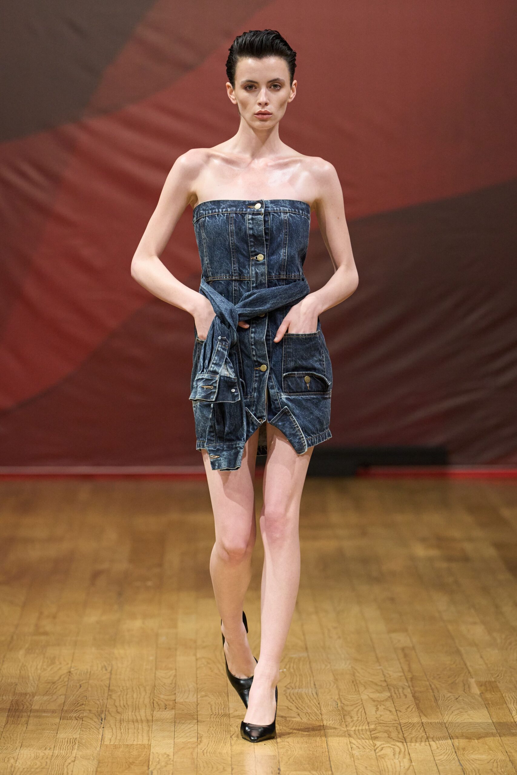 Strapless dark-wash denim mini, corseted with brass shank buttons and tied sleeves at the waist. Black leather pumps with a narrow pointed toe. Whatever you wear to cross a varnished hall after midnight cleanup.