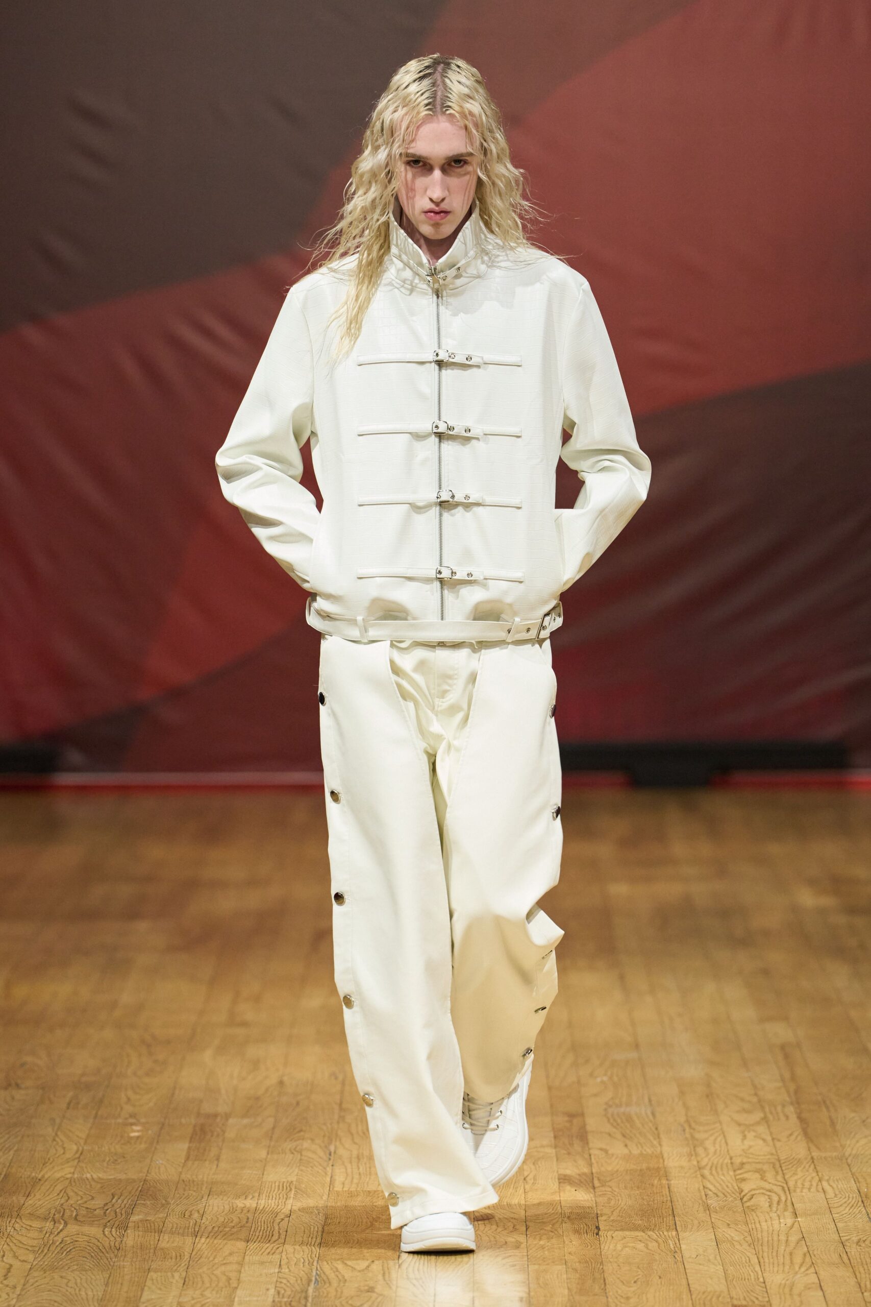 Milk-white jacket with a stand collar, zip front and strapped metal bars. Matching wide trousers, side seams opening in snap-fastened slits. White low-top sneakers with a quilted vamp. Walking the long hall outside a private clinic after visiting hours.