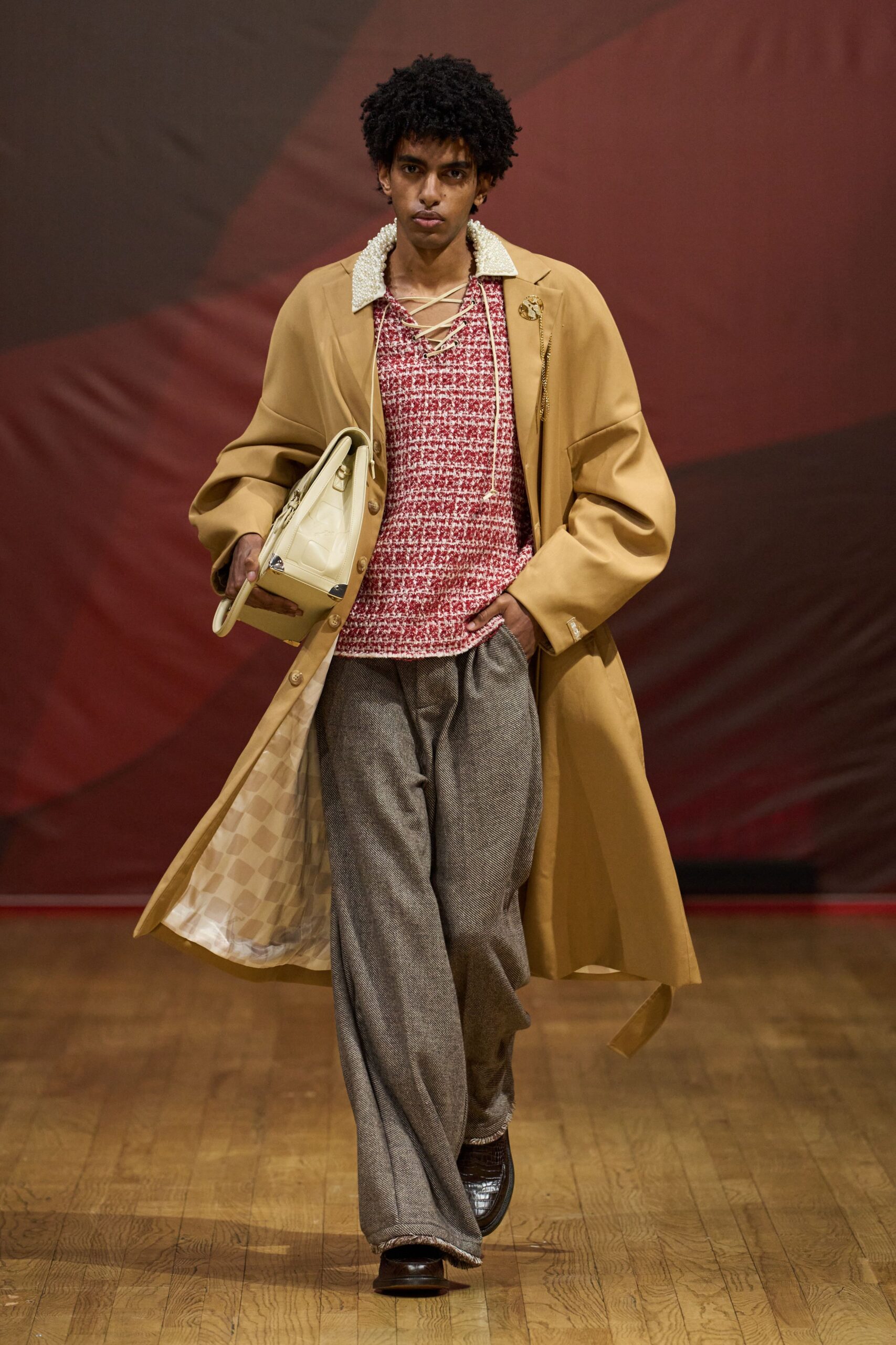 Camel overcoat with a pearl-beaded collar and checked lining. Red-and-cream bouclé top, neckline crisscrossed with long cream laces. Grey herringbone wide-legs breaking over the shoe. Buttercream top-handle bag with silver corner caps. Dark crocodile-embossed leather shoes. For arriving at a hotel bar before your room is ready.