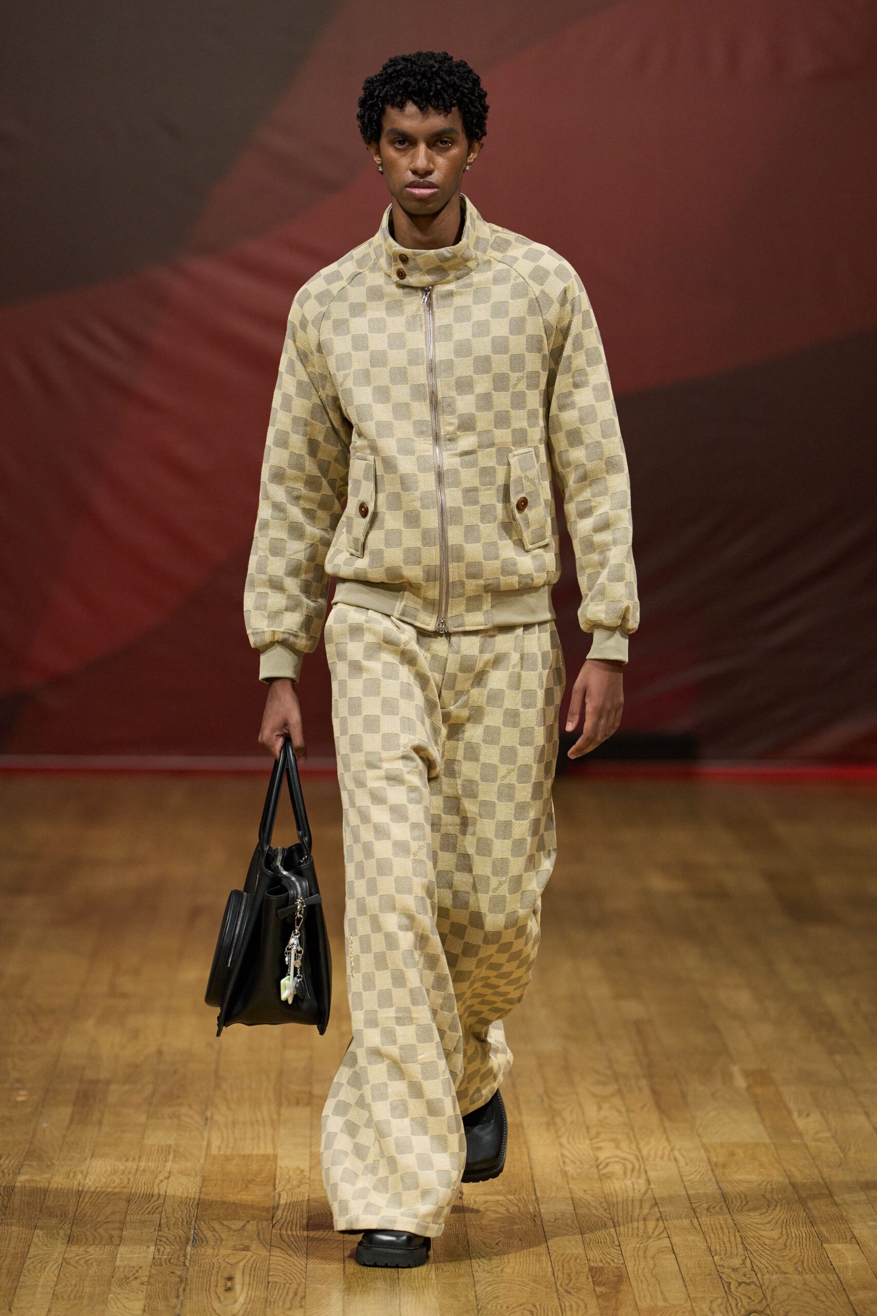 Cream and taupe checker jacquard jacket with a zipped funnel neck. Matching wide-leg trousers pooling over the shoe tops. Structured black leather tote with dangling shell charms. Black square-toe shoes with heavy lug soles. Walking into a seaside hotel lobby before anyone changes for dinner.