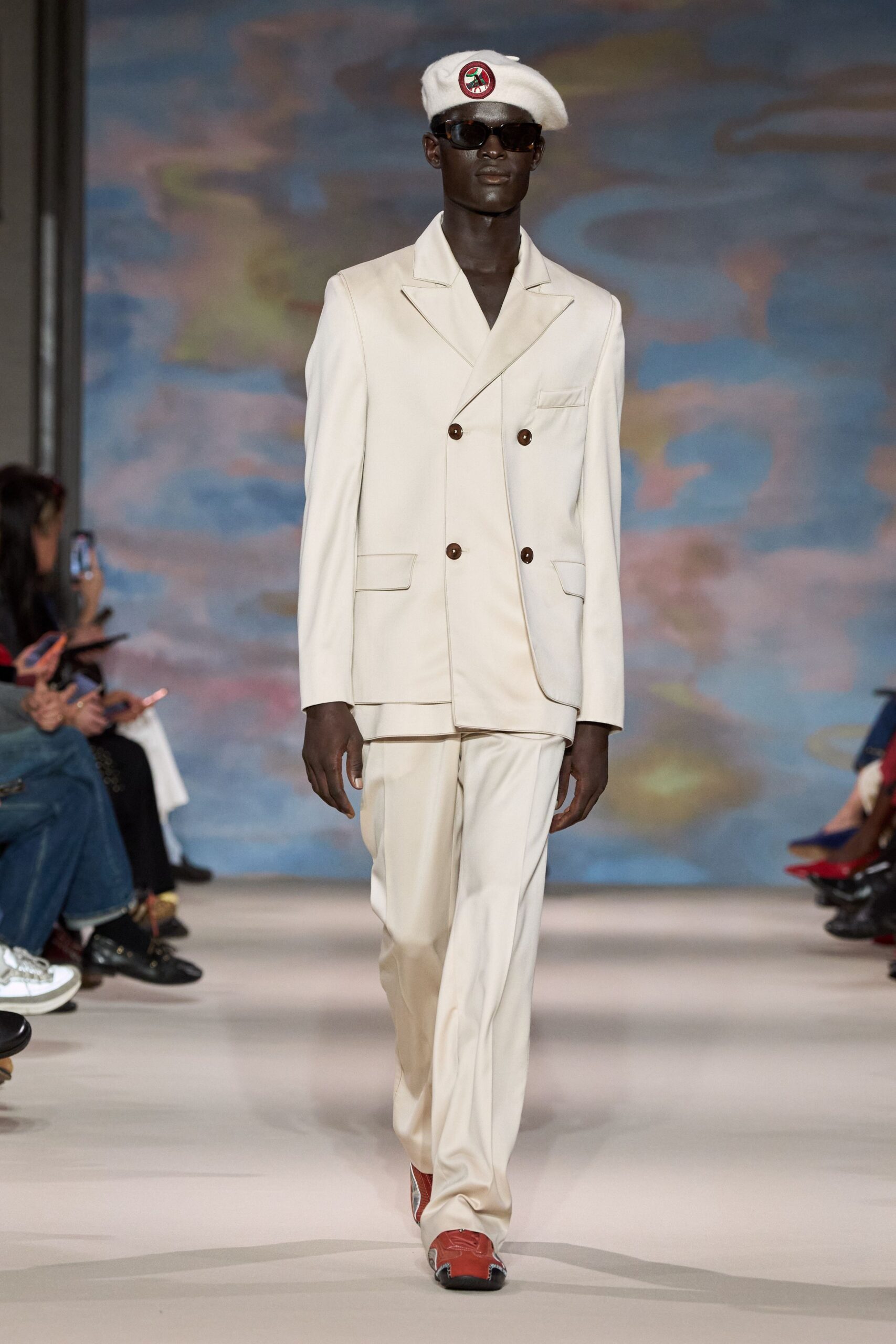 White wool beret with a circular stitched badge. Dark rectangular frames. Cream tailoring with brown buttons and a slightly dropped hem. Cream trousers breaking softly over the shoe. Rust leather shoes with white contrast trim at the toe. Sunday ferry terminal, still dressed for lunch onshore.