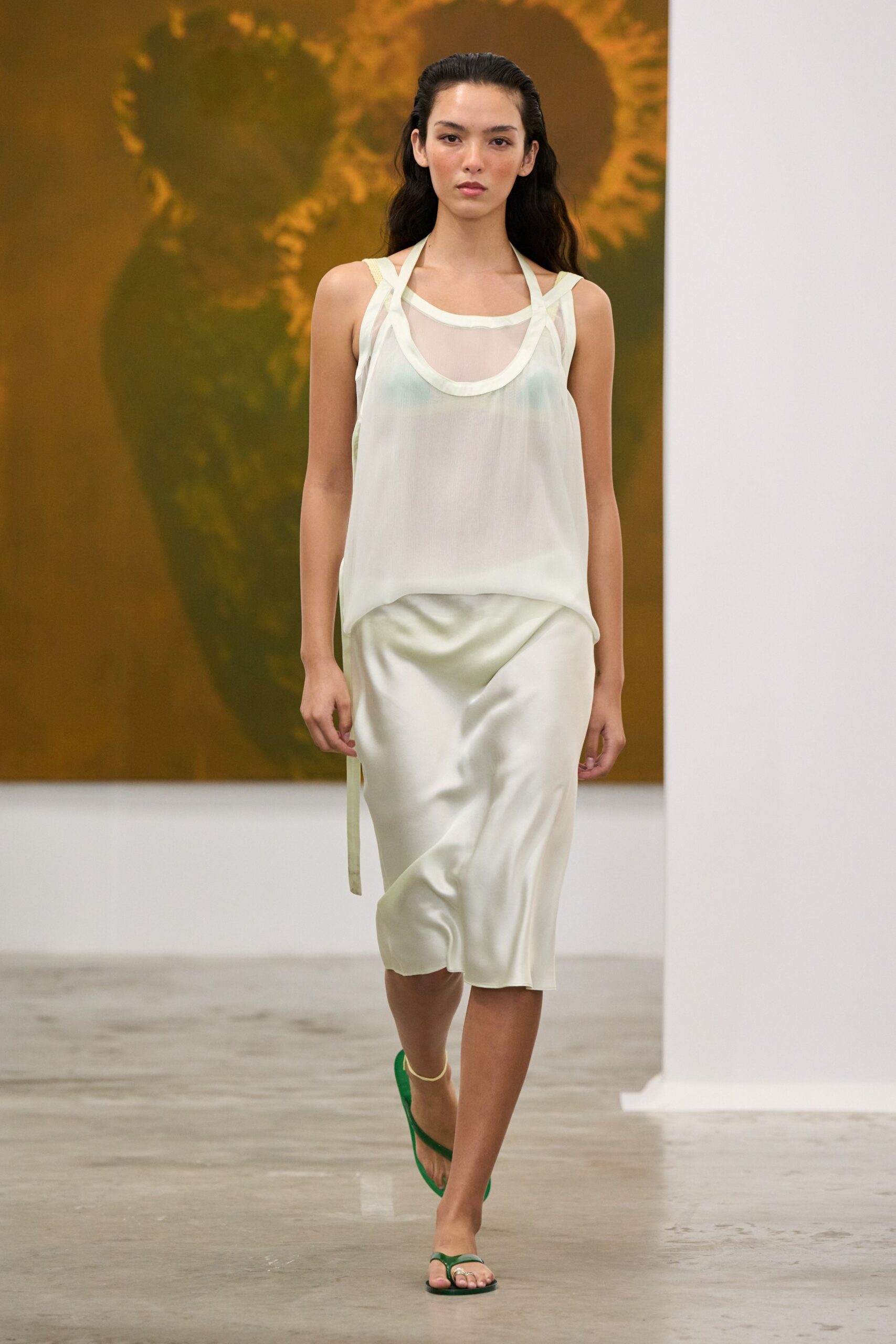 Sheer ivory chiffon tank, doubled neckline looping into narrow shoulder straps. Pearly bias-cut satin slip skirt with a ribbon tab hanging at the hip. Green thong sandals. Walking barefoot-adjacent through a rental house the morning after a beach wedding.