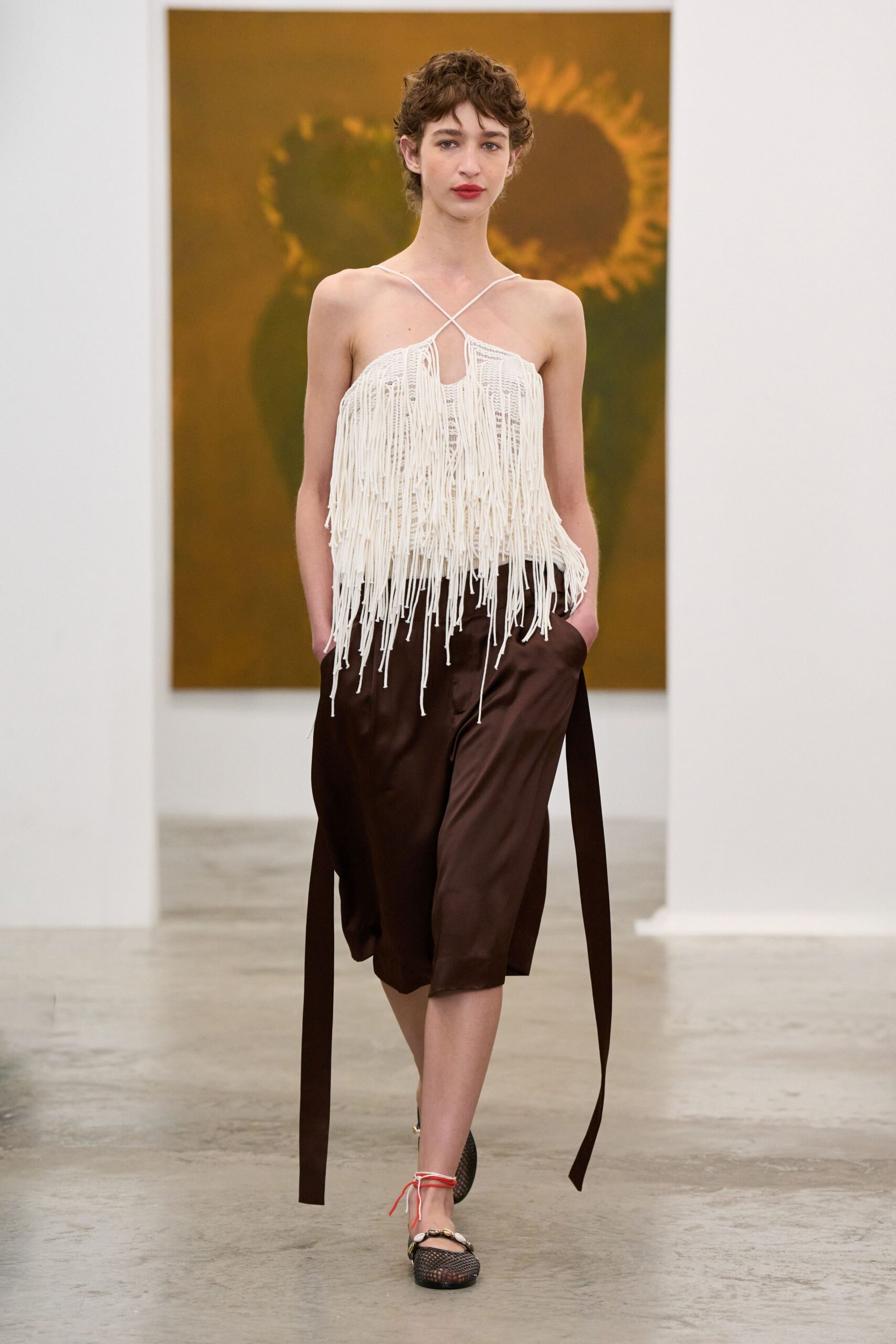 Ivory knit halter top buried under long swaying fringe cords. Chocolate satin culottes with ribbon ties hanging past the knee. Black mesh flats with shell trim and coral ankle laces. Walking through a quiet museum after the school groups have gone.