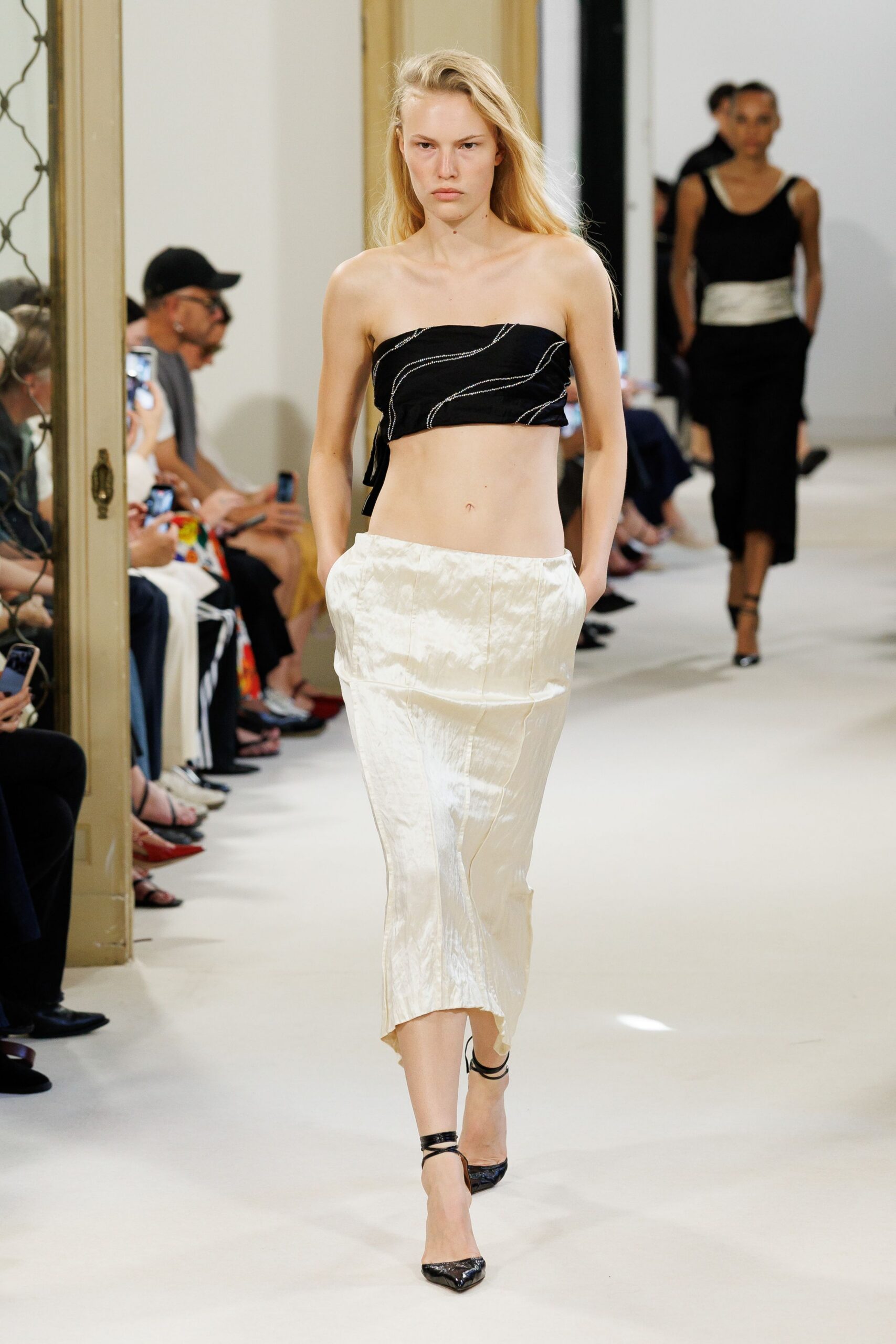 Black bandeau with silver beaded squiggles and a side tie. Ivory crushed satin pencil skirt, low on the hip with pockets. Black patent pumps laced at the ankle. Crossing a hotel lobby barefoot in your head, heels clicking anyway.
