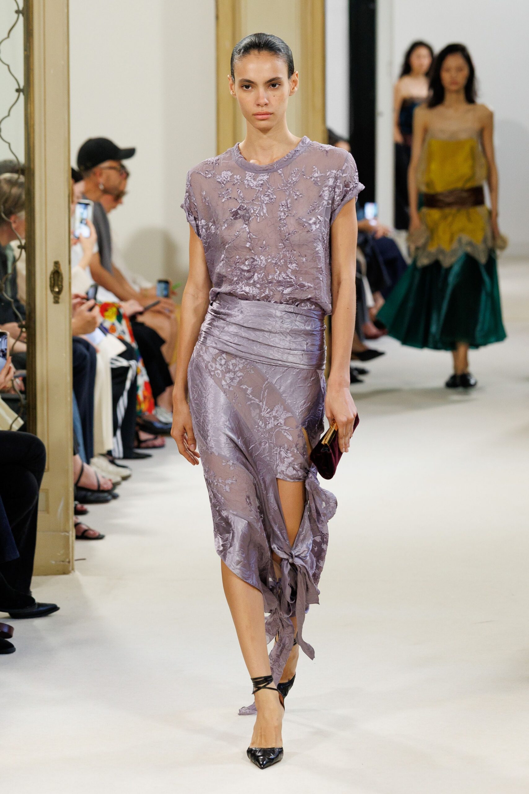 Lilac devore top, sheer through the torso with rolled cap sleeves. Matching bias skirt, ruched waistband and a slit knotted into trailing strips. Burgundy velvet clutch with a slim gold frame. Black patent heels with winding ankle straps. Whatever you wear to cross a hotel lobby before breakfast is served.