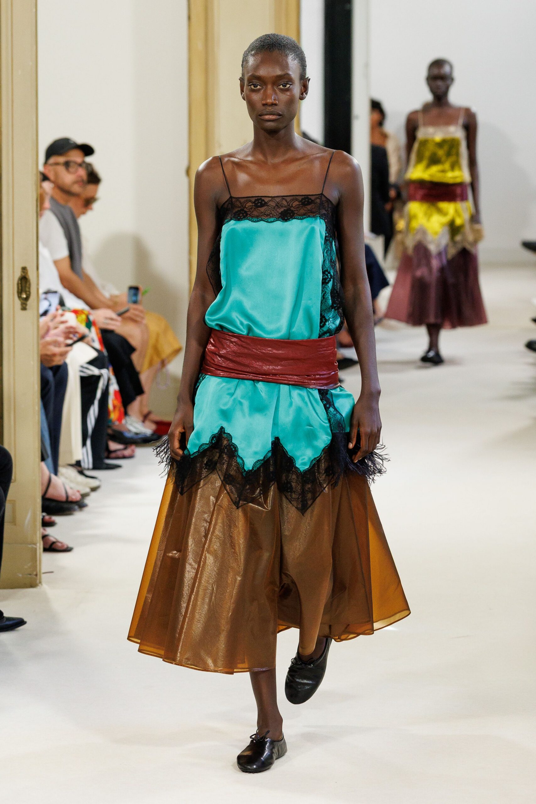 Turquoise satin slip with black lace inset and feathery points at the hem. Oxblood leather wrapped low and ruched into a broad sash. Copper organza midi, sheer and belling away from the knees. Black leather ballet flats with a tiny bow knot. Walking back from a hotel wedding with the corsage already gone.