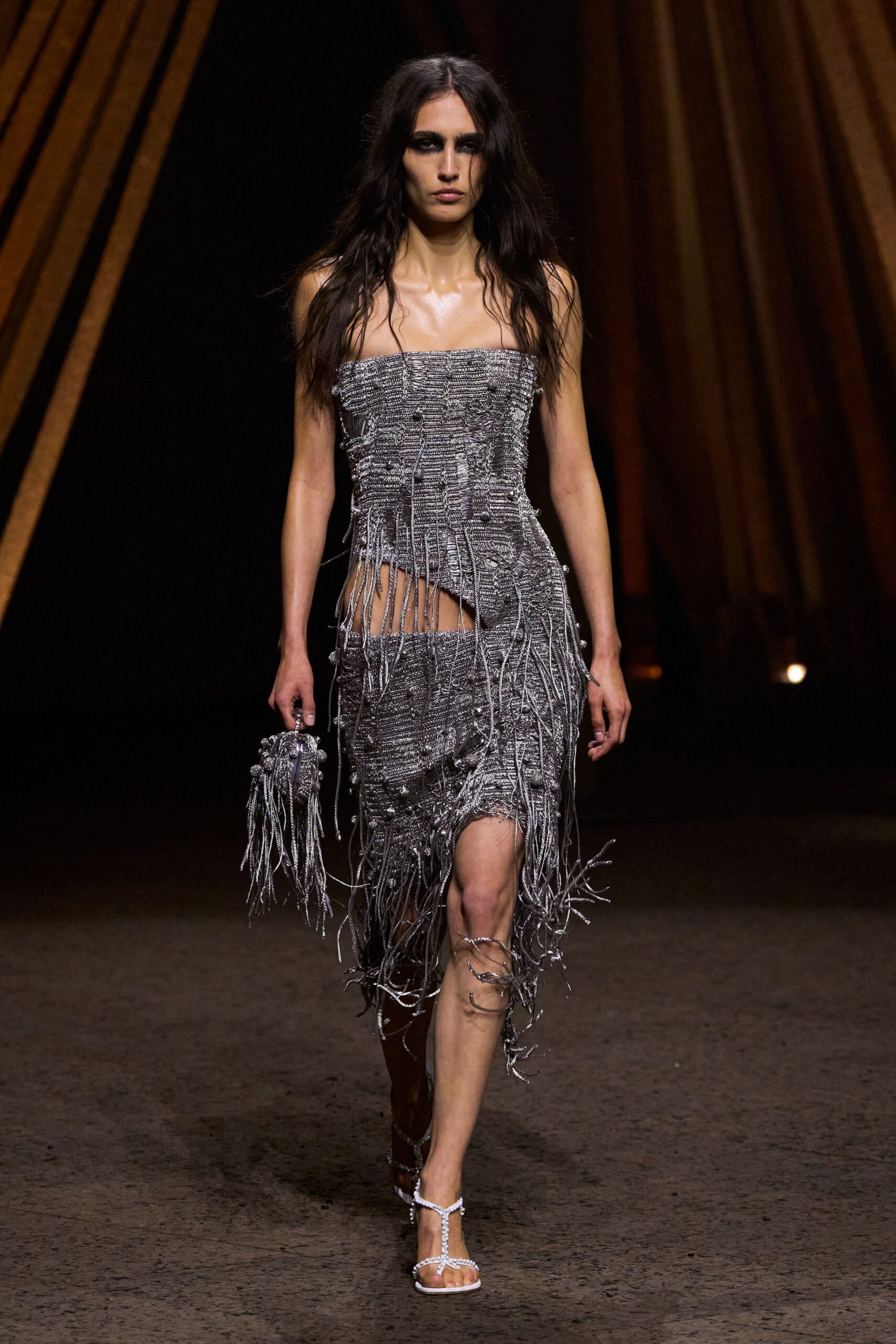 Silver bandeau dress in nubbly fringe-knit, sliced open at one hip. Matching tasselled pouch, gripped by a ring handle. White thong heels with crystal cords spiralling up one calf. Walking out of a hotel ballroom after the band has packed up.